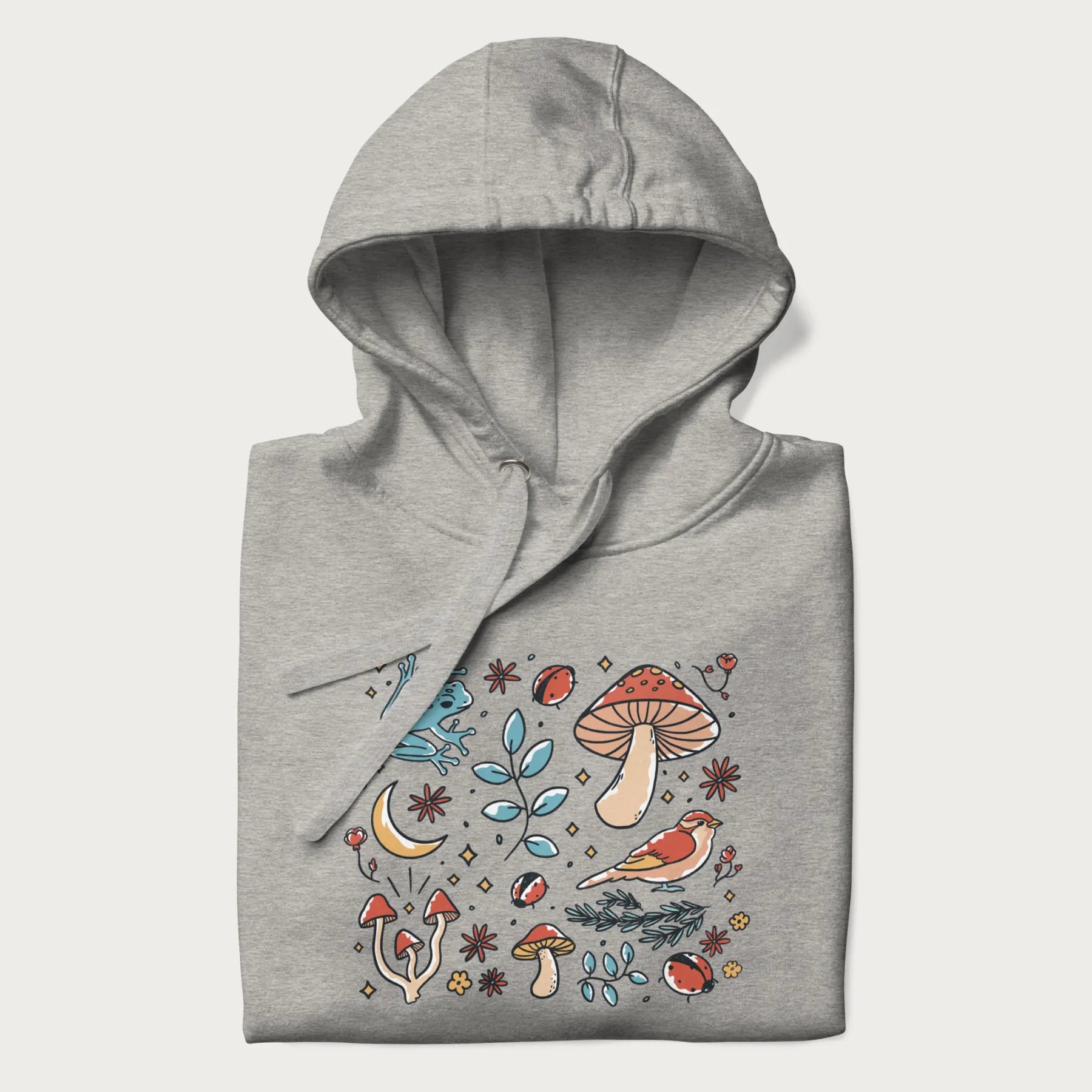 Folded light grey hoodie with a graphic of a blue frog, mushrooms, a bird, ladybugs, flowers, leaves, and a crescent moon.