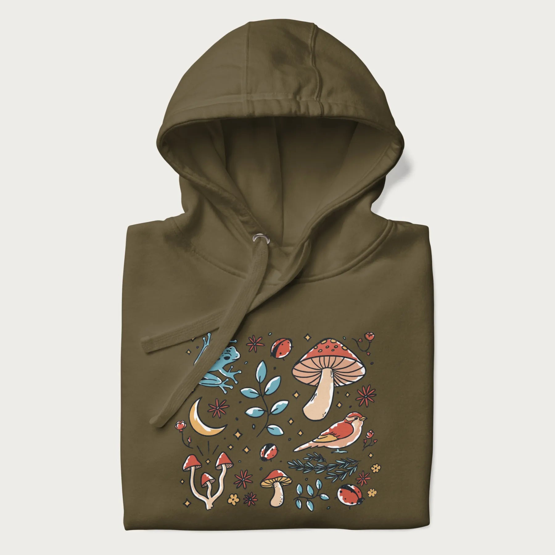 Folded military green hoodie with a graphic of a blue frog, mushrooms, a bird, ladybugs, flowers, leaves, and a crescent moon.