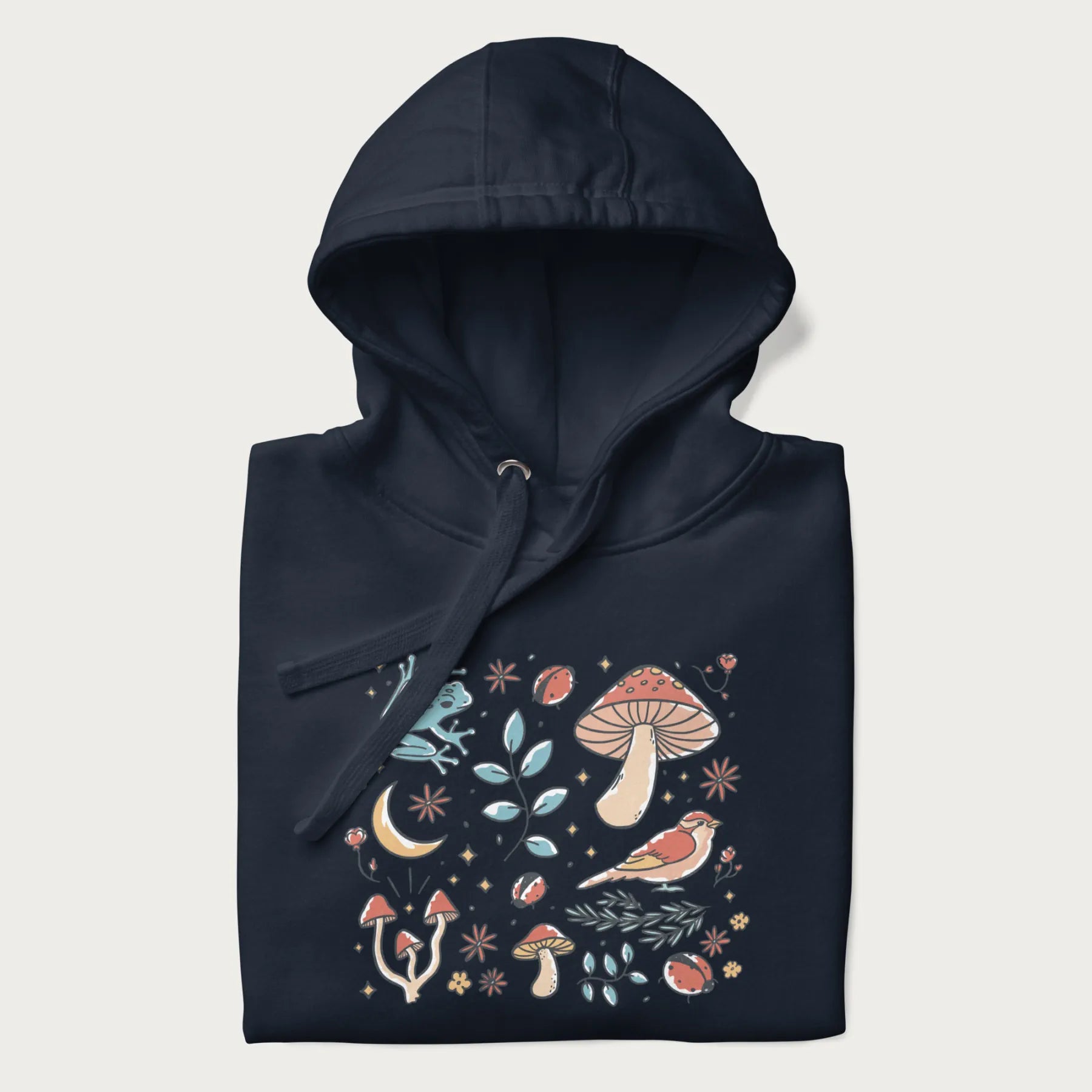 Folded navy blue hoodie with a graphic of a blue frog, mushrooms, a bird, ladybugs, flowers, leaves, and a crescent moon.