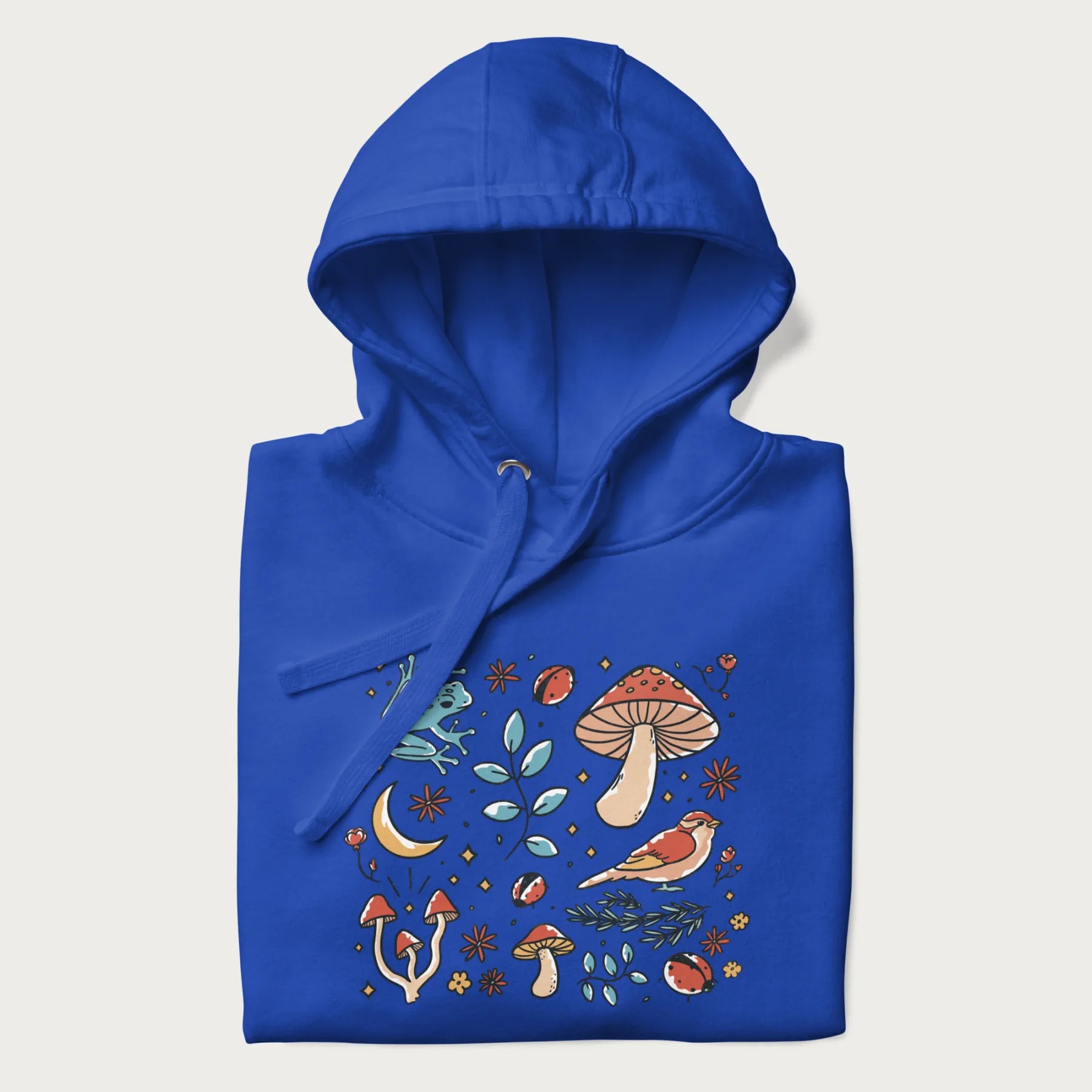 Folded royal blue hoodie with a graphic of a blue frog, mushrooms, a bird, ladybugs, flowers, leaves, and a crescent moon.