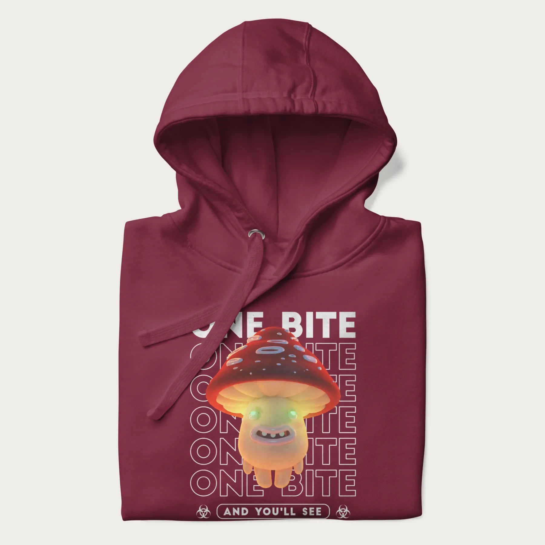 Folded maroon hoodie with a graphic of a glowing, cartoon realistic mushroom character and the text 'One Bite And You'll See'.