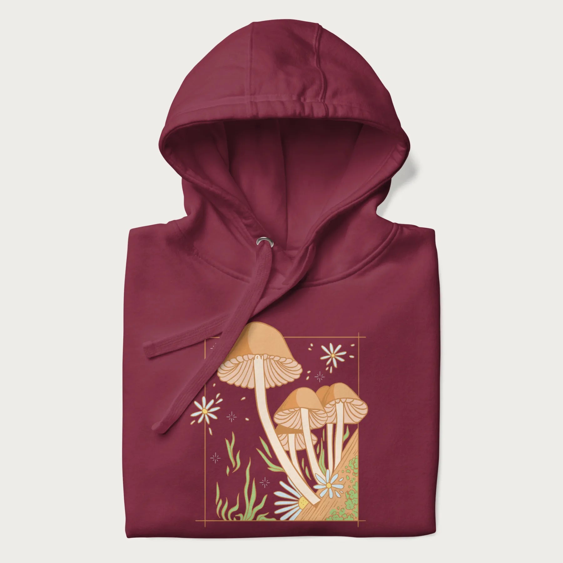 Folded maroon hoodie with a detailed cottagecore illustration of Psilocybe mushrooms and flowers.