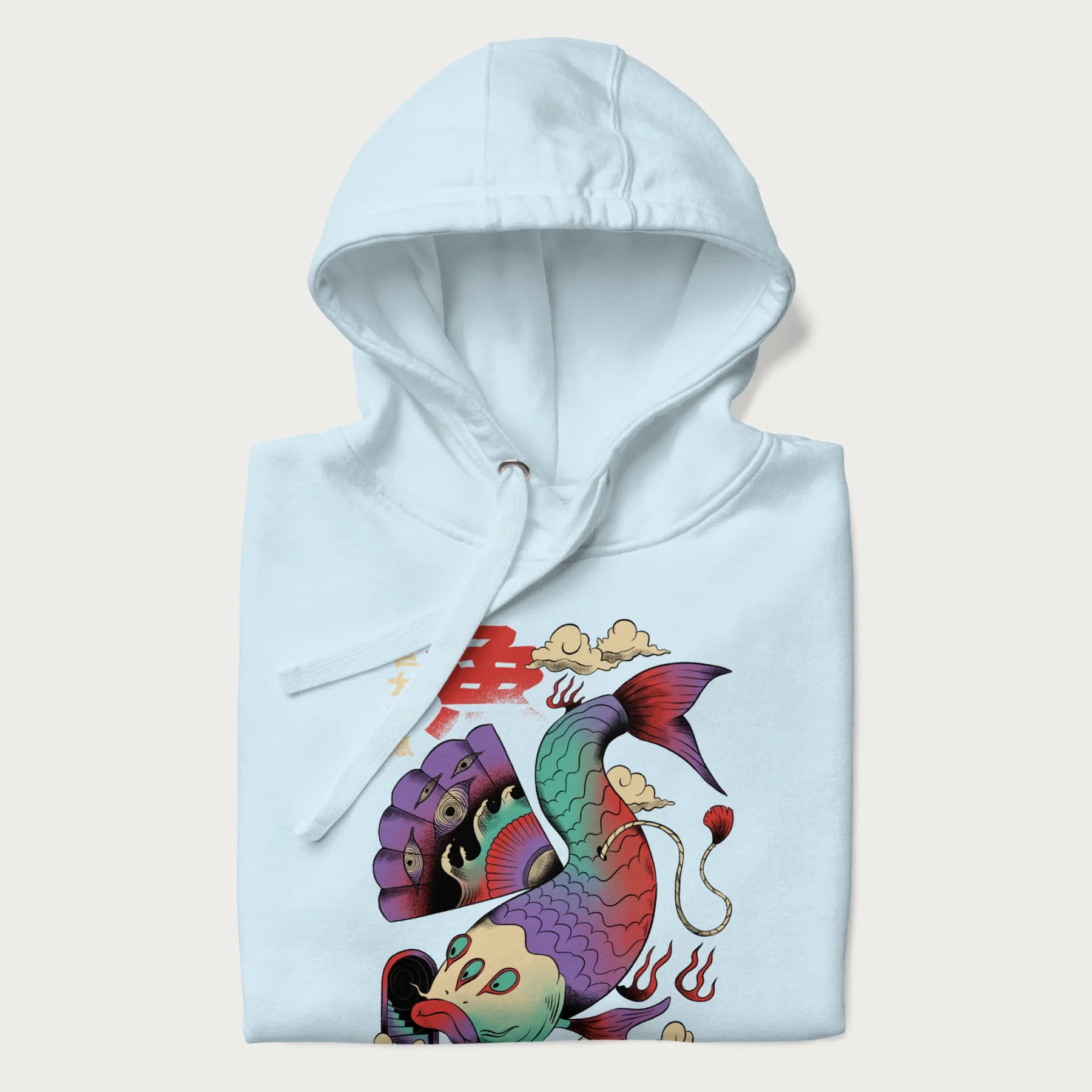 Folded light blue hoodie with Japanese graphic of a colorful psychedelic koi fish, with Japanese text '魚' (Fish) and '巨大な魚' (Giant Fish).