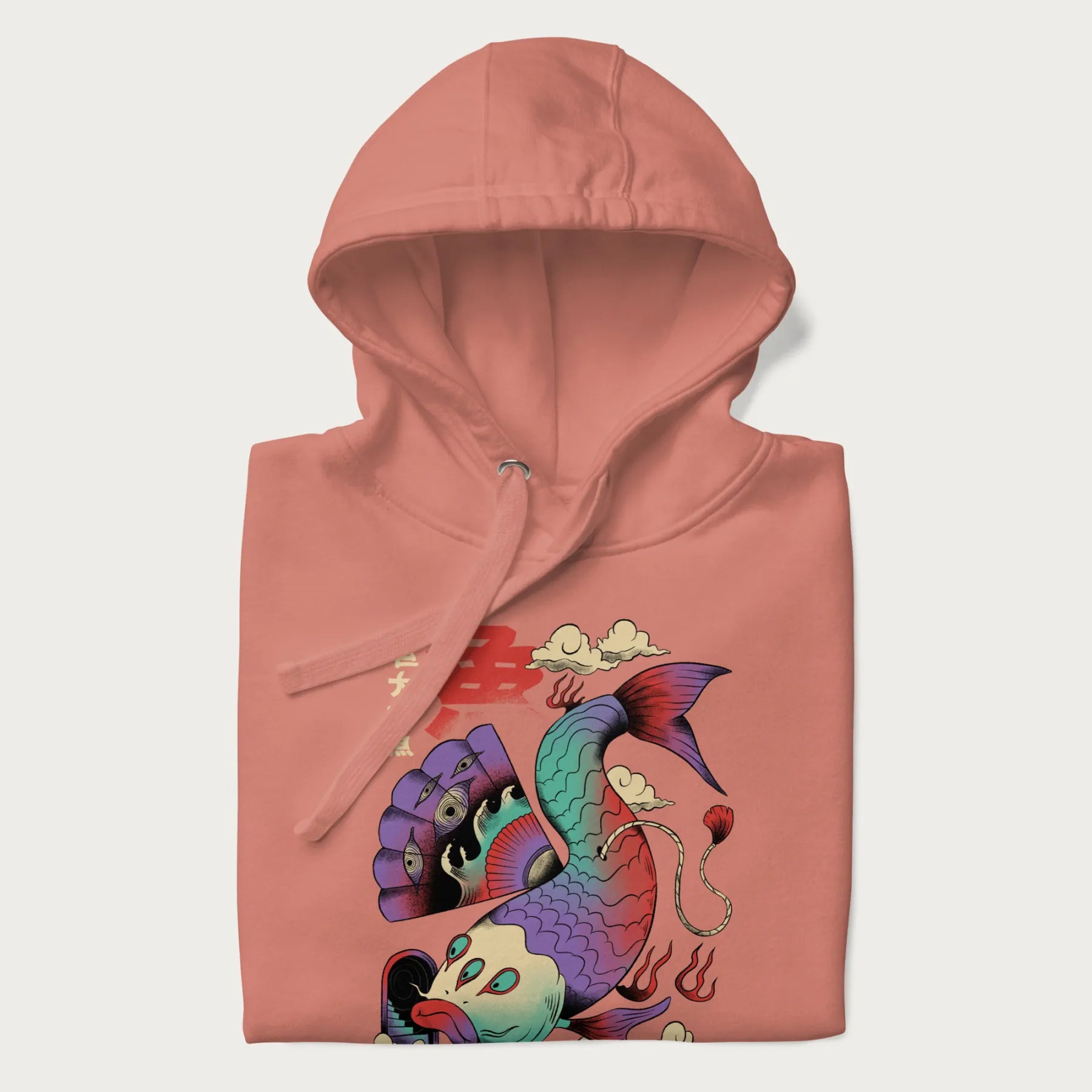 Folded light pink hoodie with Japanese graphic of a colorful psychedelic koi fish, with Japanese text '魚' (Fish) and '巨大な魚' (Giant Fish).