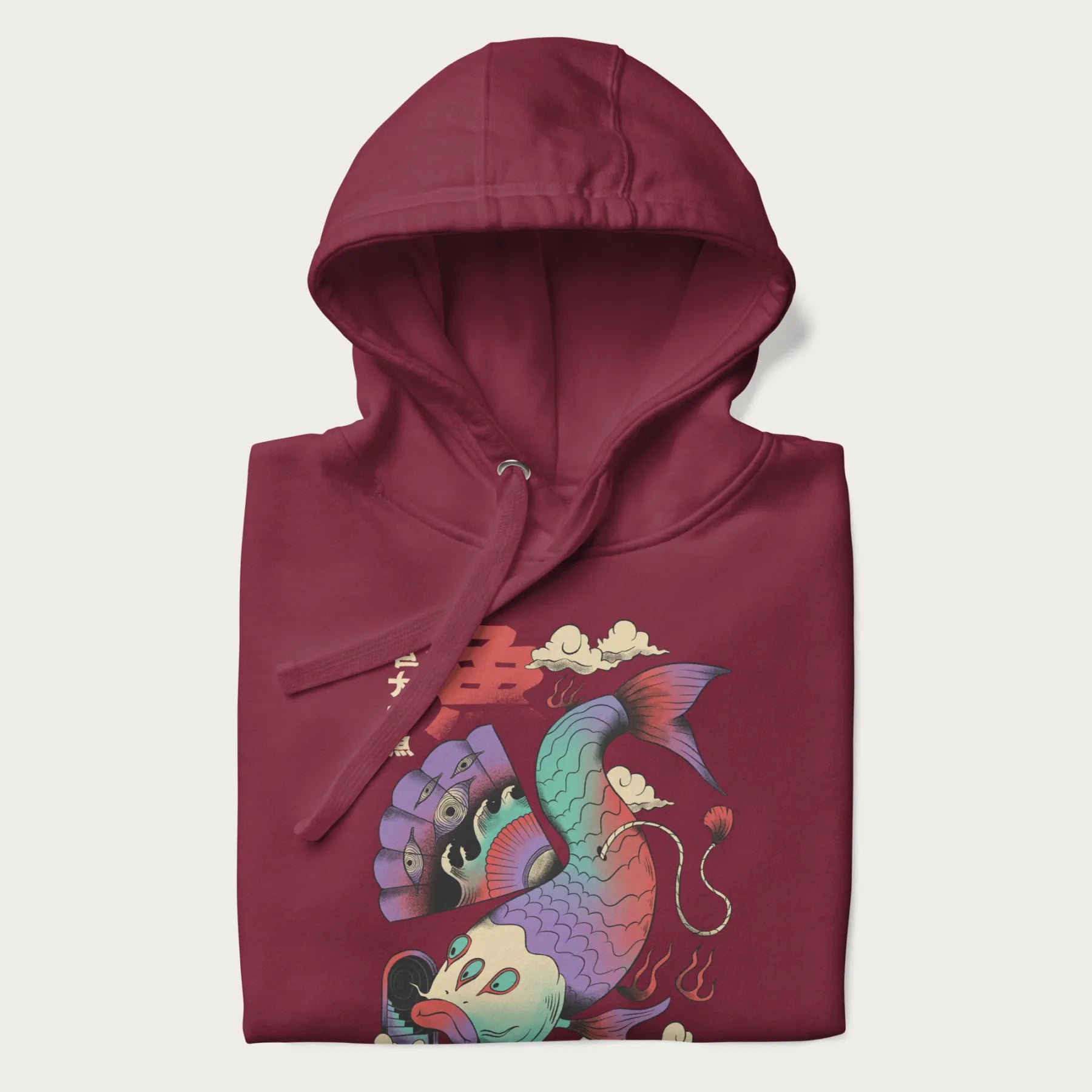 Folded maroon hoodie with Japanese graphic of a colorful psychedelic koi fish, with Japanese text '魚' (Fish) and '巨大な魚' (Giant Fish).