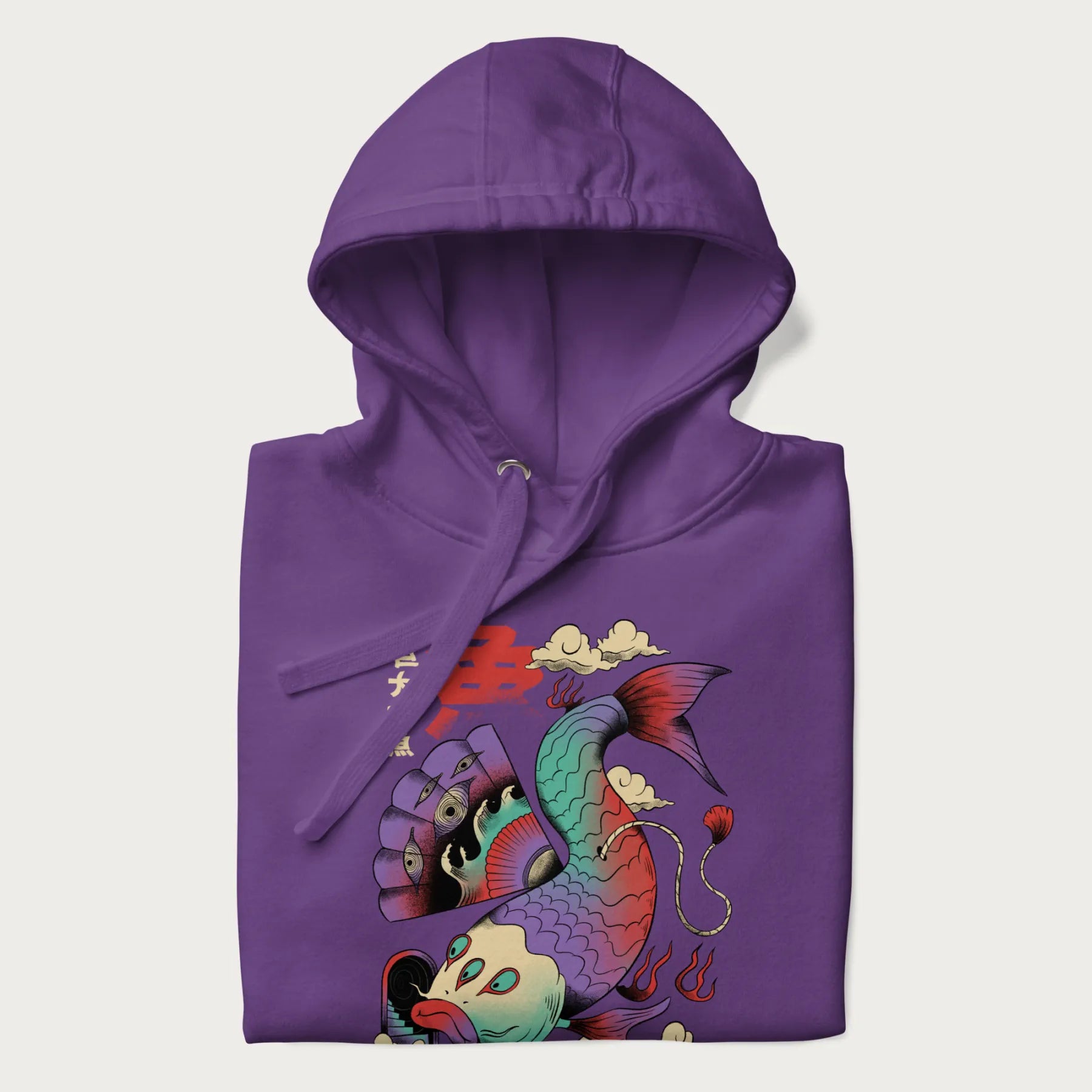 Folded purple hoodie with Japanese graphic of a colorful psychedelic koi fish, with Japanese text '魚' (Fish) and '巨大な魚' (Giant Fish).