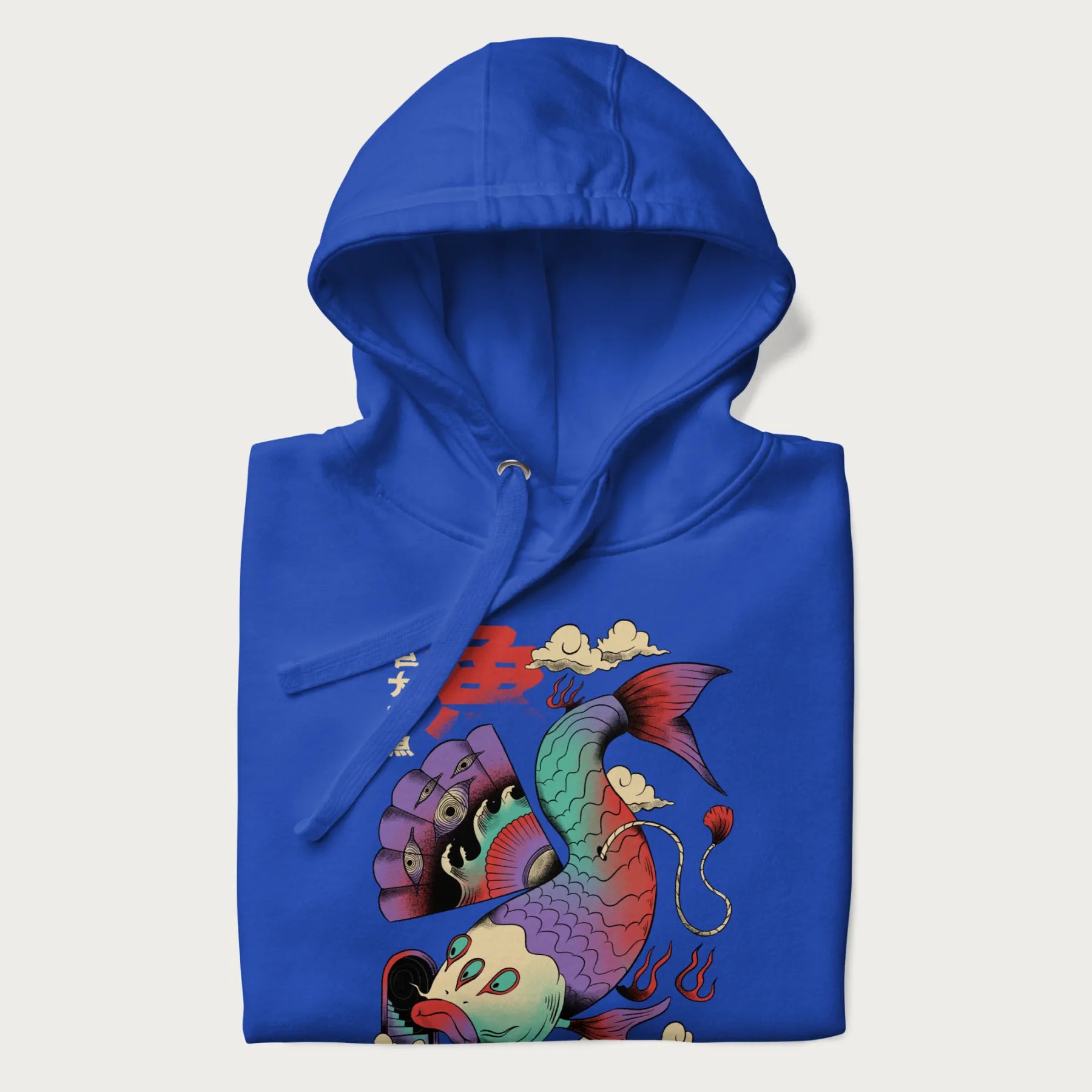 Folded royal blue hoodie with Japanese graphic of a colorful psychedelic koi fish, with Japanese text '魚' (Fish) and '巨大な魚' (Giant Fish).