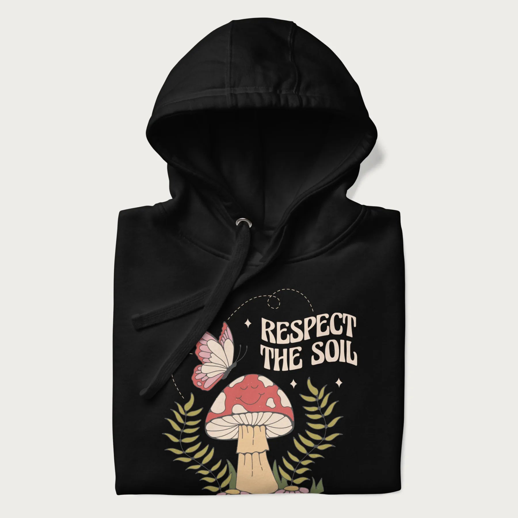 Folded black hoodie with mushroom and butterfly design, with the text 'Respect the Soil' above it.