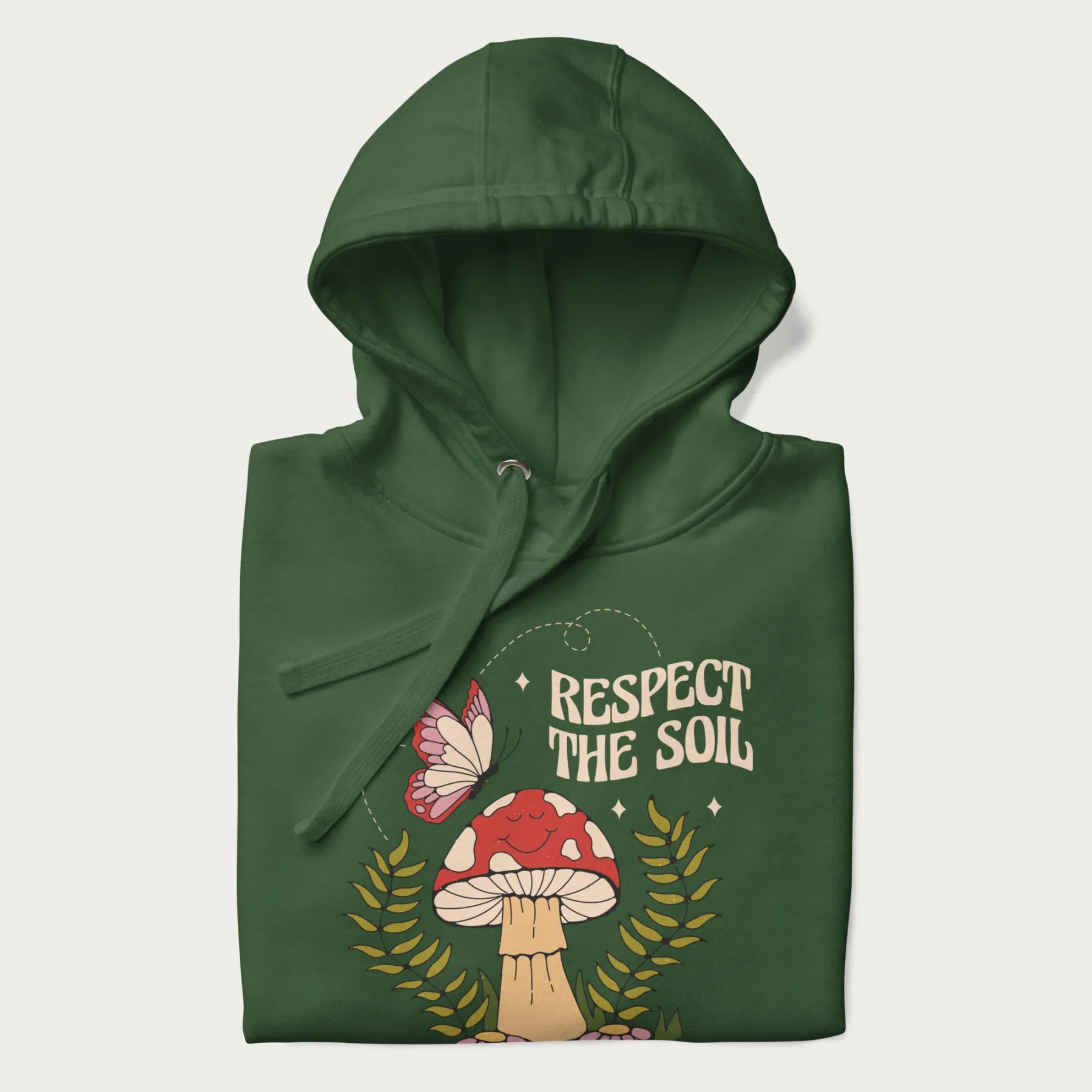 Folded forest green hoodie with mushroom and butterfly design, with the text 'Respect the Soil' above it.