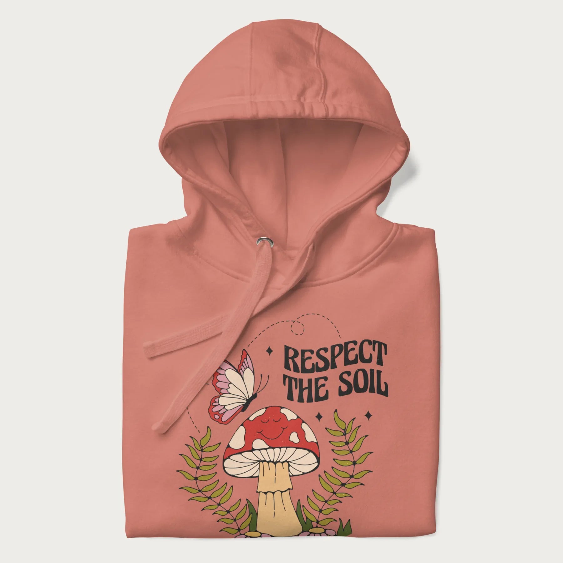 Folded light pink hoodie with mushroom and butterfly design, with the text 'Respect the Soil' above it.