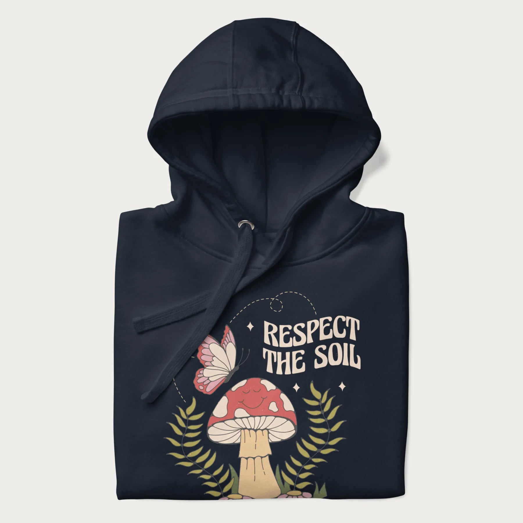 Folded navy blue hoodie with mushroom and butterfly design, with the text 'Respect the Soil' above it.