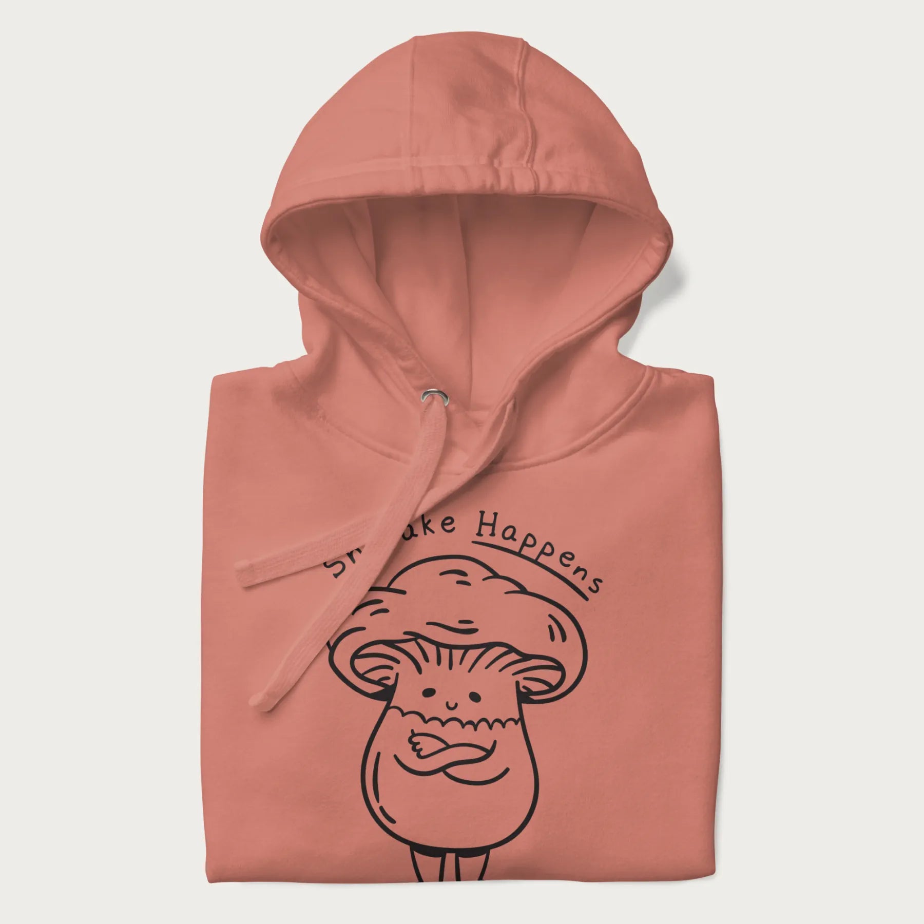 Folded light pink hoodie featuring a cute shiitake mushroom graphic with the text "Shiitake Happens."