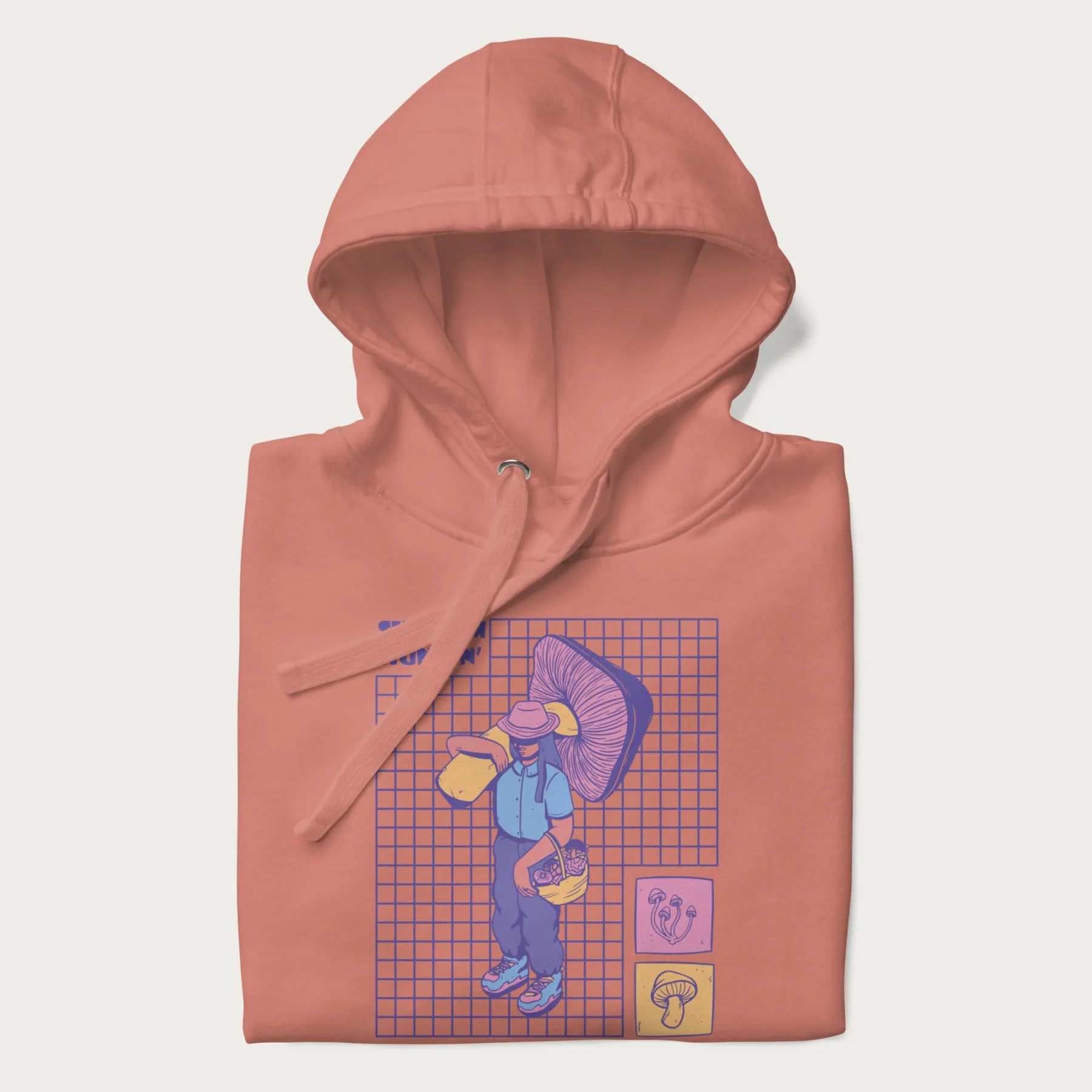 Folded light pink hoodie featuring a graphic of a girl carrying a large mushroom and a basket of fungi, with the text "Shroom Huntin'".