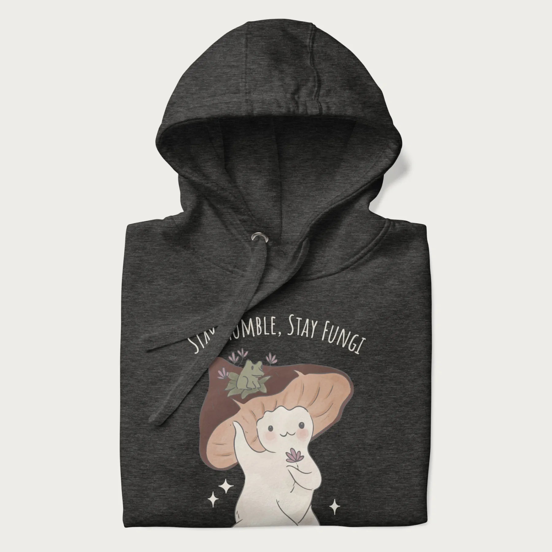 Folded dark grey hoodie with graphic of a cute mushroom character holding a flower with a frog on its cap and the text 'Stay Humble, Stay Fungi' above.