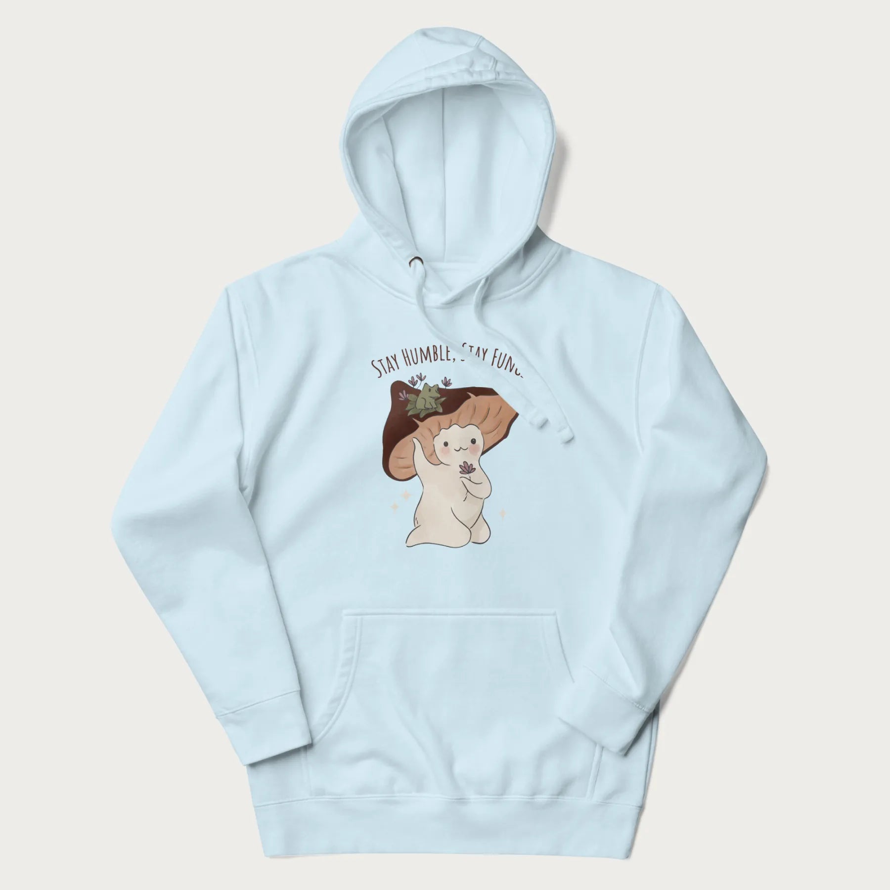 Light blue hoodie with graphic of a cute mushroom character holding a flower with a frog on its cap and the text 'Stay Humble, Stay Fungi' above.