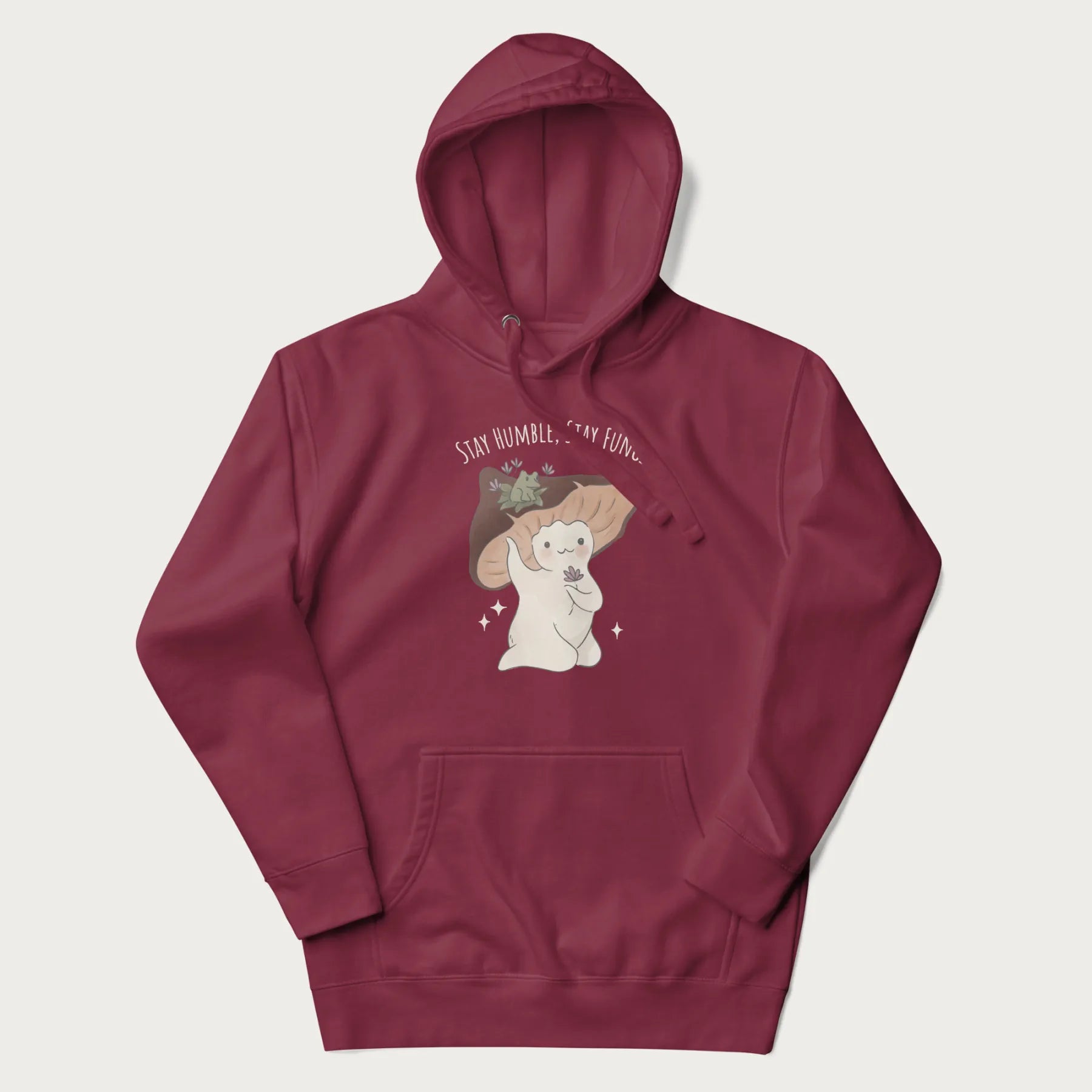 Maroon hoodie with graphic of a cute mushroom character holding a flower with a frog on its cap and the text 'Stay Humble, Stay Fungi' above.