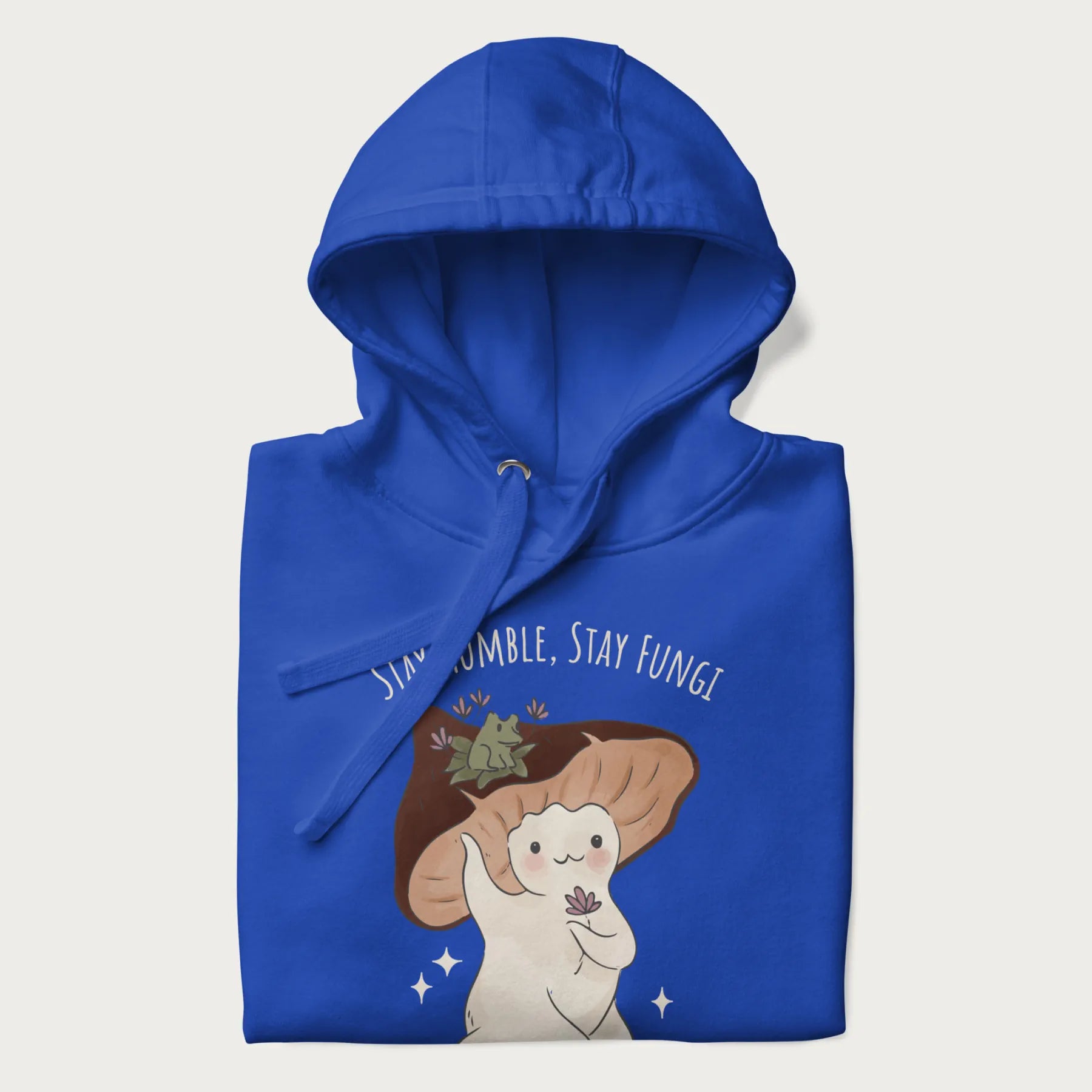 Folded royal blue hoodie with graphic of a cute mushroom character holding a flower with a frog on its cap and the text 'Stay Humble, Stay Fungi' above.