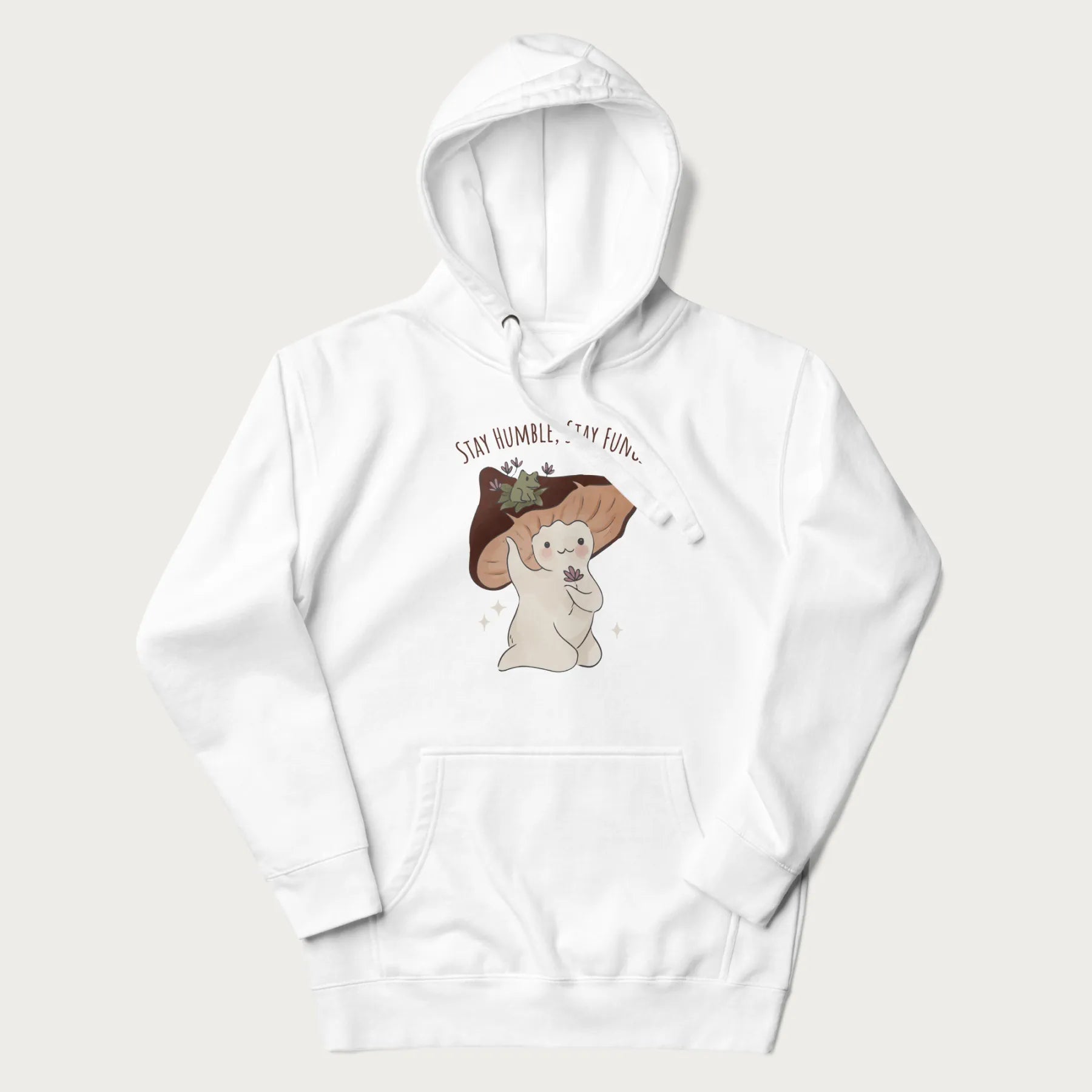 White hoodie with graphic of a cute mushroom character holding a flower with a frog on its cap and the text 'Stay Humble, Stay Fungi' above.