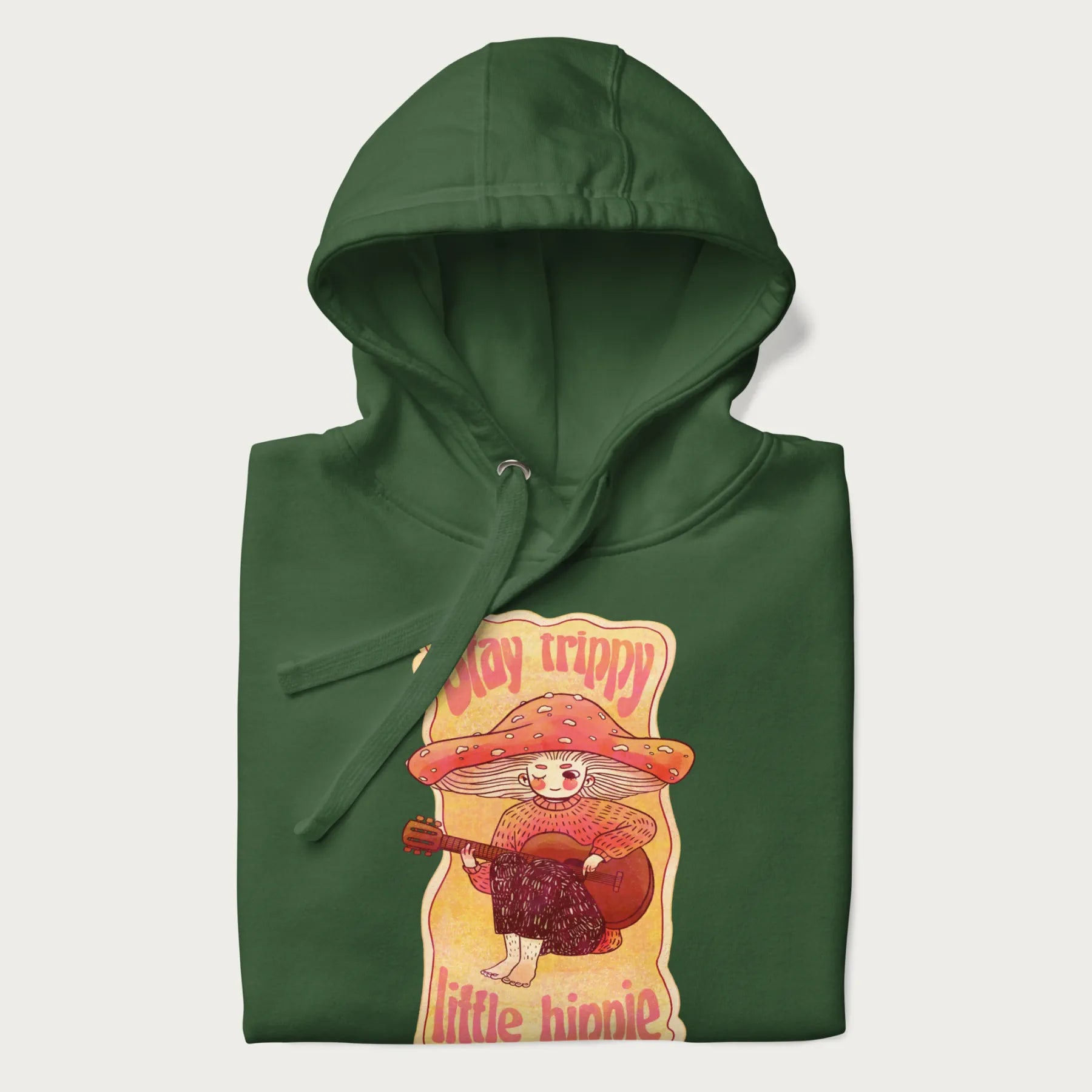 Folded forest green hoodie with a graphic of a character with a mushroom cap playing a guitar and the text 'Stay Trippy Little Hippie.'