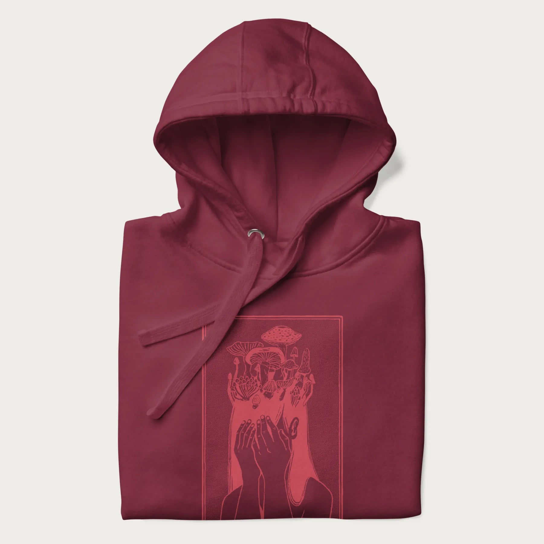 Folded maroon hoodie with a surreal red graphic of a girl with mushrooms growing from her head.