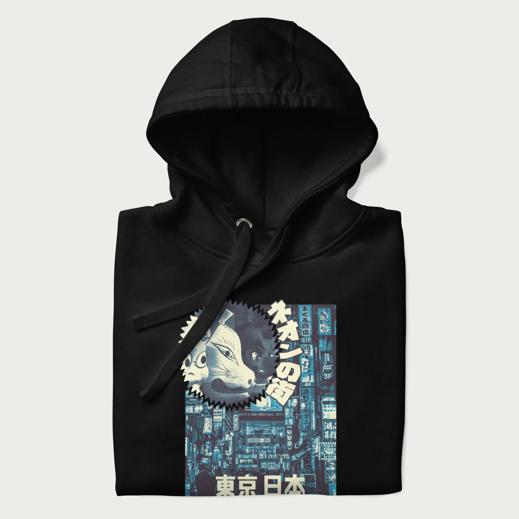 Folded black hoodie with Japanese text '東京日本' translating to 'Tokyo, Japan', with three traditional Japanese masks over a neon-lit Tokyo background.