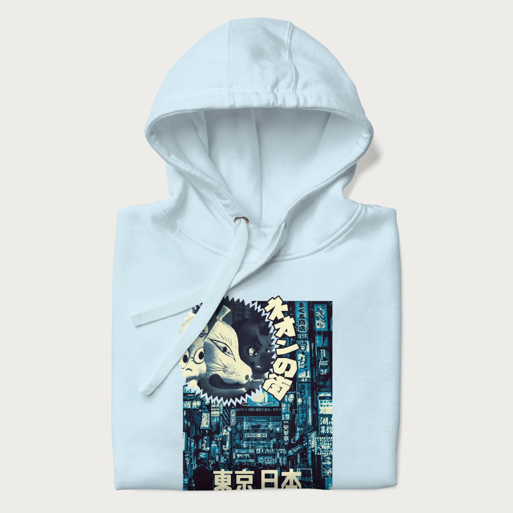 Folded light blue hoodie with Japanese text '東京日本' translating to 'Tokyo, Japan', with three traditional Japanese masks over a neon-lit Tokyo background.
