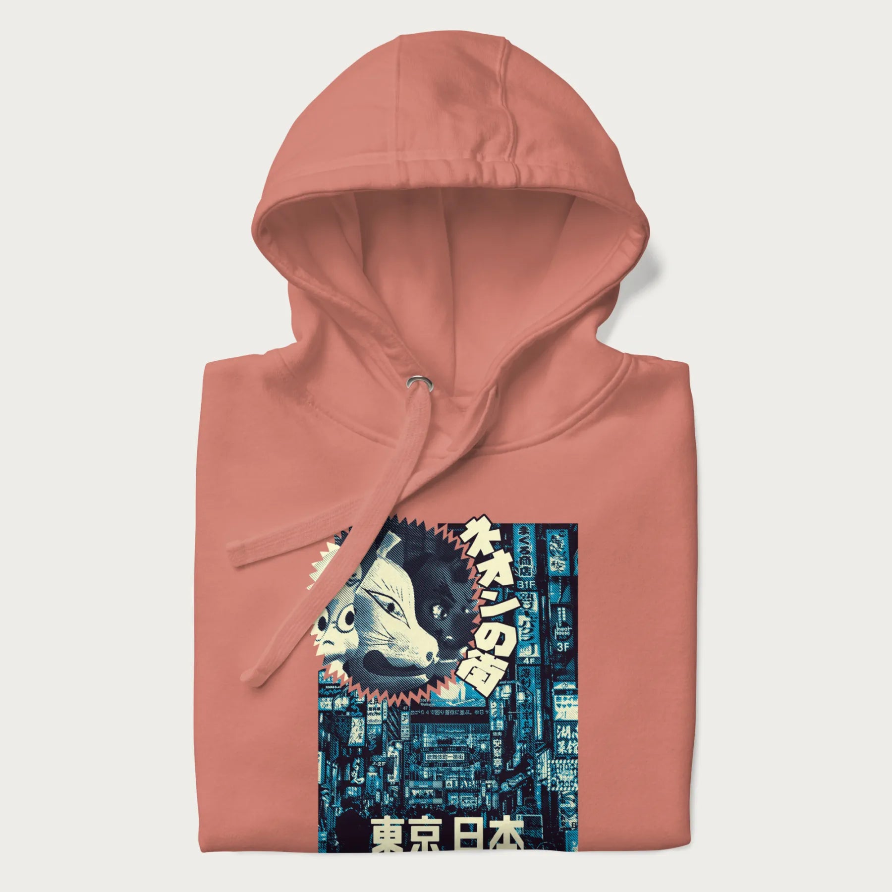 Folded light pink hoodie with Japanese text '東京日本' translating to 'Tokyo, Japan', with three traditional Japanese masks over a neon-lit Tokyo background.