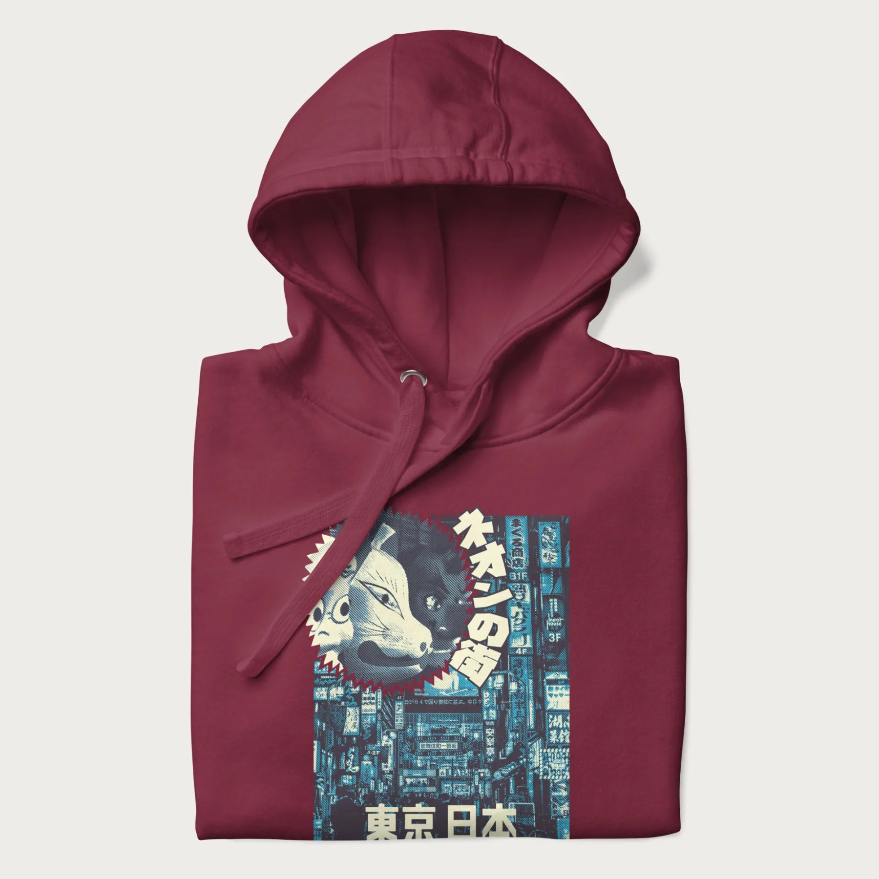 Folded maroon hoodie with Japanese text '東京日本' translating to 'Tokyo, Japan', with three traditional Japanese masks over a neon-lit Tokyo background.