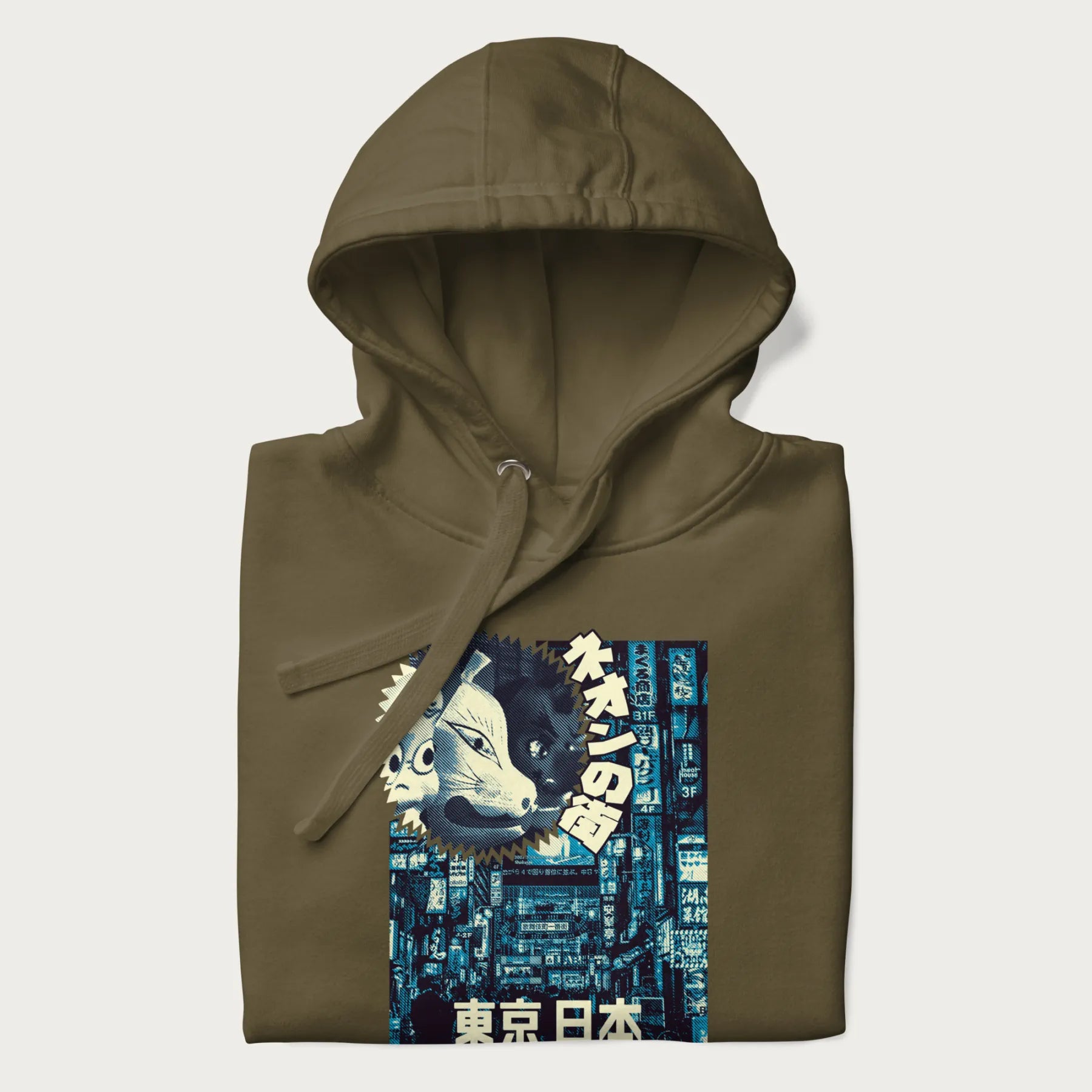 Folded military green hoodie with Japanese text '東京日本' translating to 'Tokyo, Japan', with three traditional Japanese masks over a neon-lit Tokyo background.