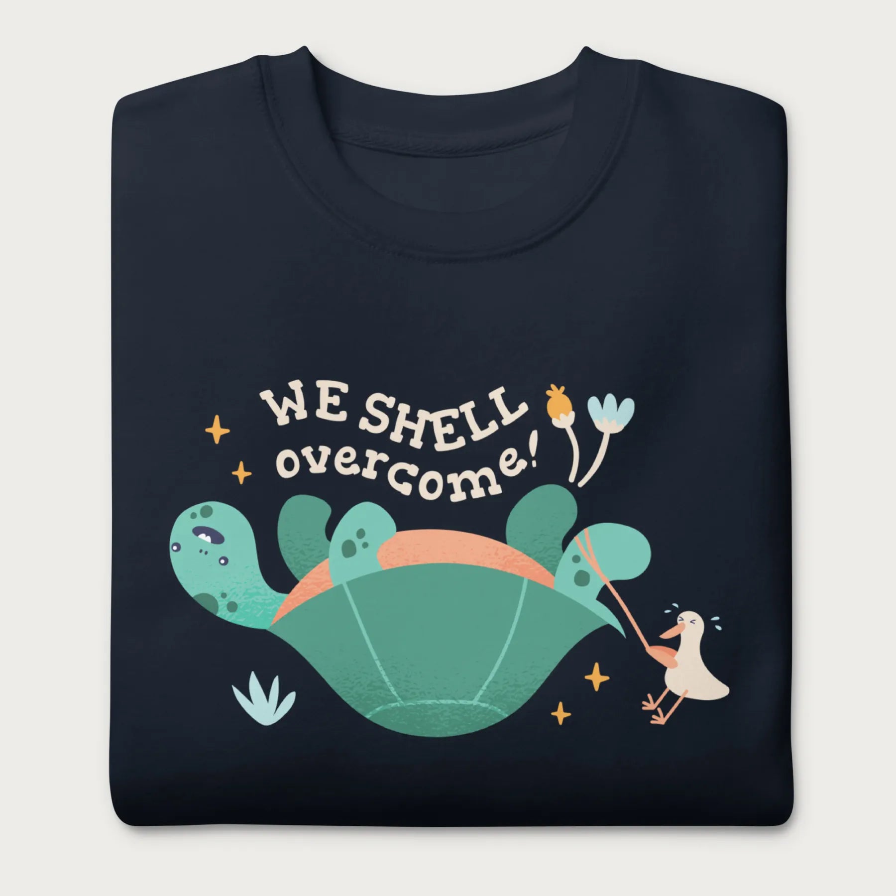 Folded navy blue sweatshirt with a graphic of a turtle flipped on it's shell with the phrase 'We Shell Overcome.'