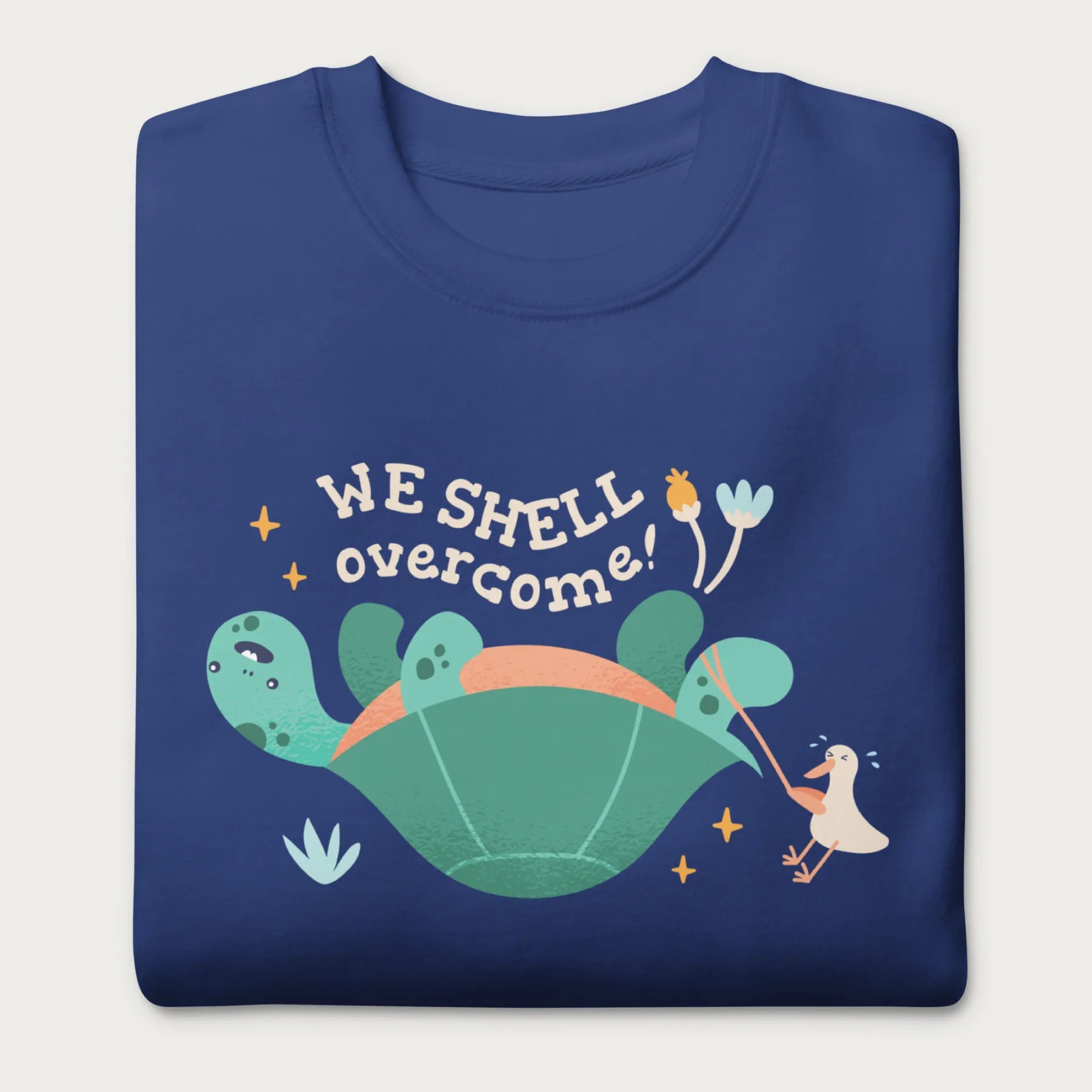 Folded royal blue sweatshirt with a graphic of a turtle flipped on it's shell with the phrase 'We Shell Overcome.'