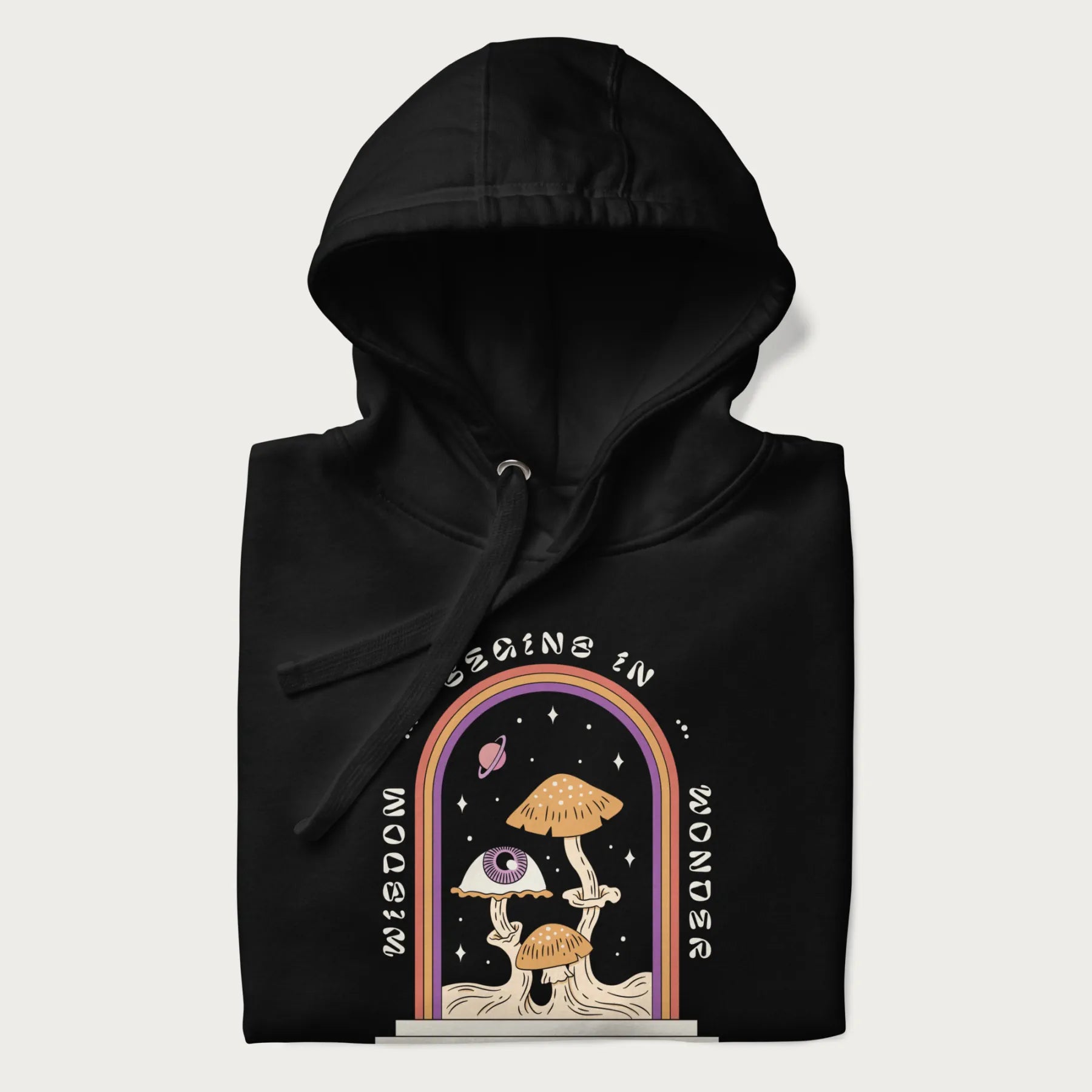 Folded black hoodie with graphic of mystical mushrooms with an all-seeing eye and the text 'Wisdom Begins in Wonder' framed by a rainbow arch.