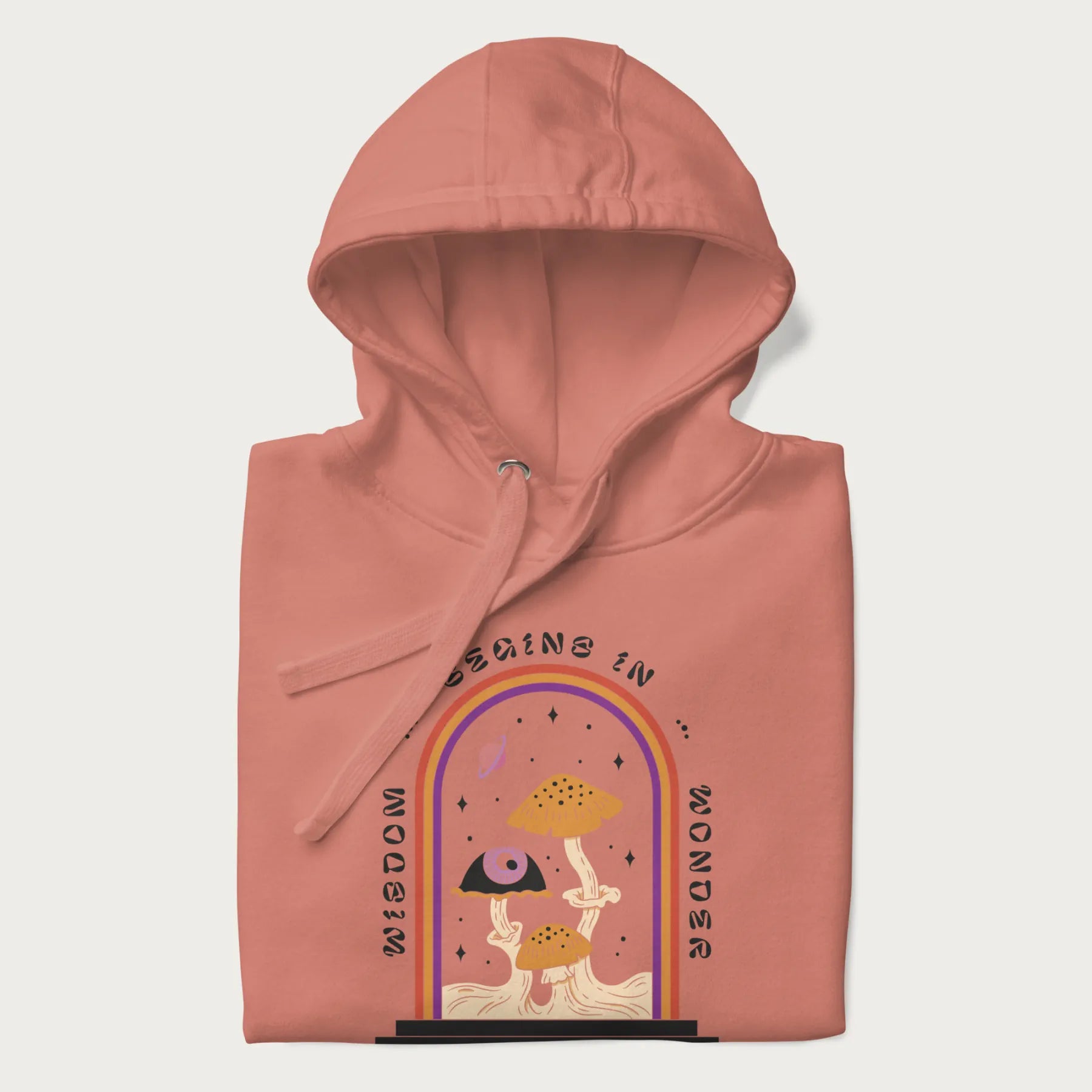 Folded light pink hoodie with graphic of mystical mushrooms with an all-seeing eye and the text 'Wisdom Begins in Wonder' framed by a rainbow arch.