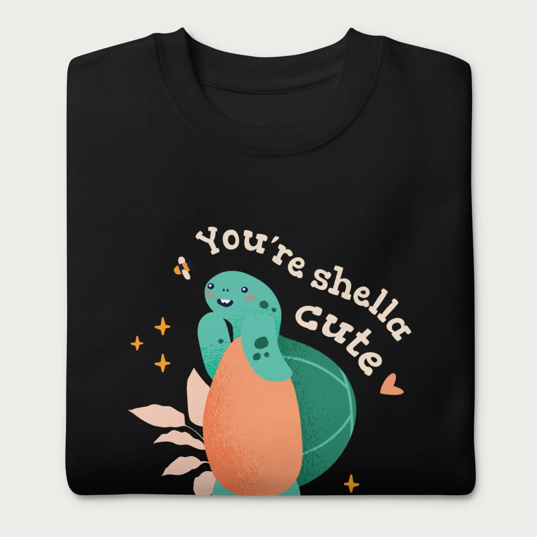Folded black sweatshirt with a cute graphic of a smiling turtle and bee with the phrase 'You're Shella Cute.'