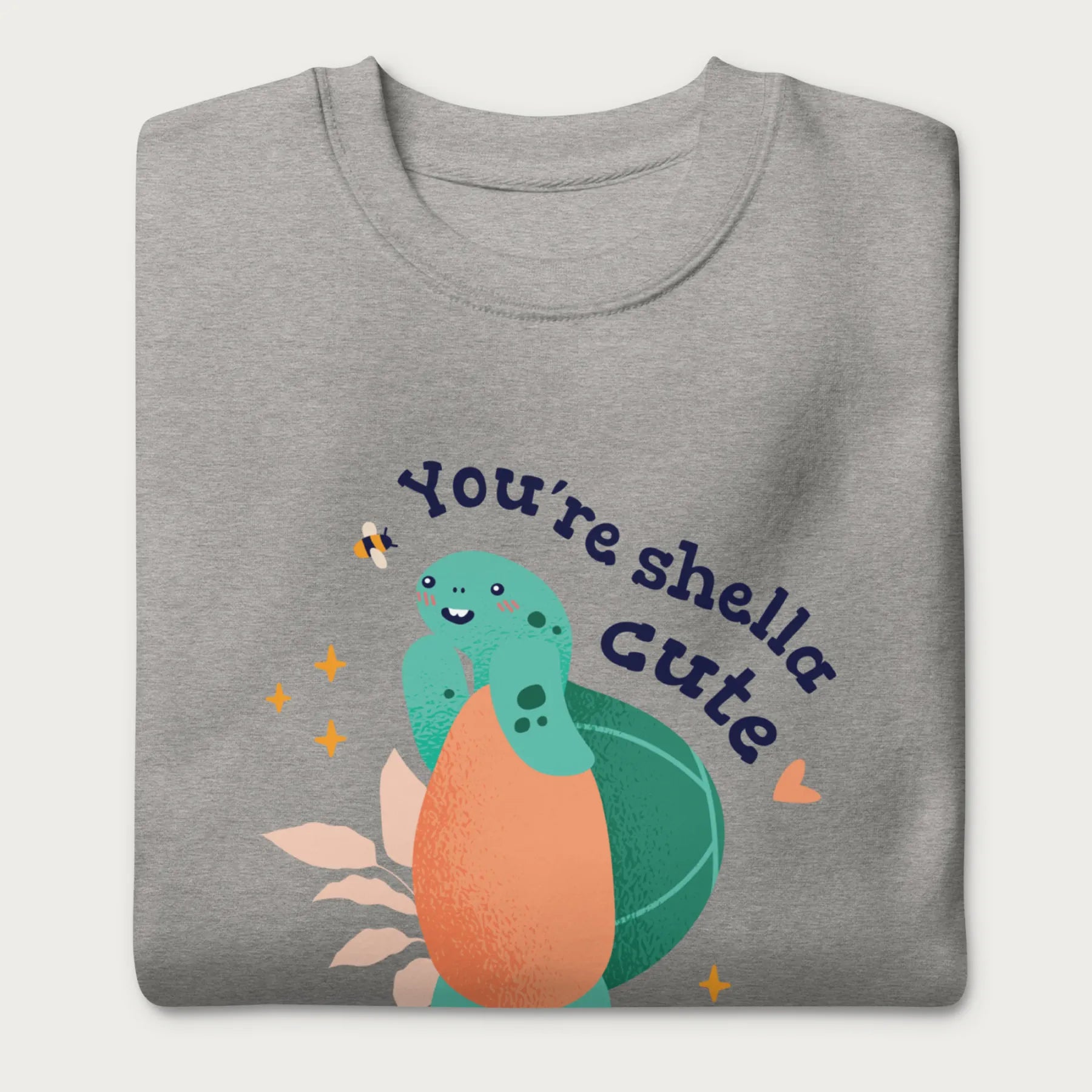 Folded light grey sweatshirt with a cute graphic of a smiling turtle and bee with the phrase 'You're Shella Cute.'