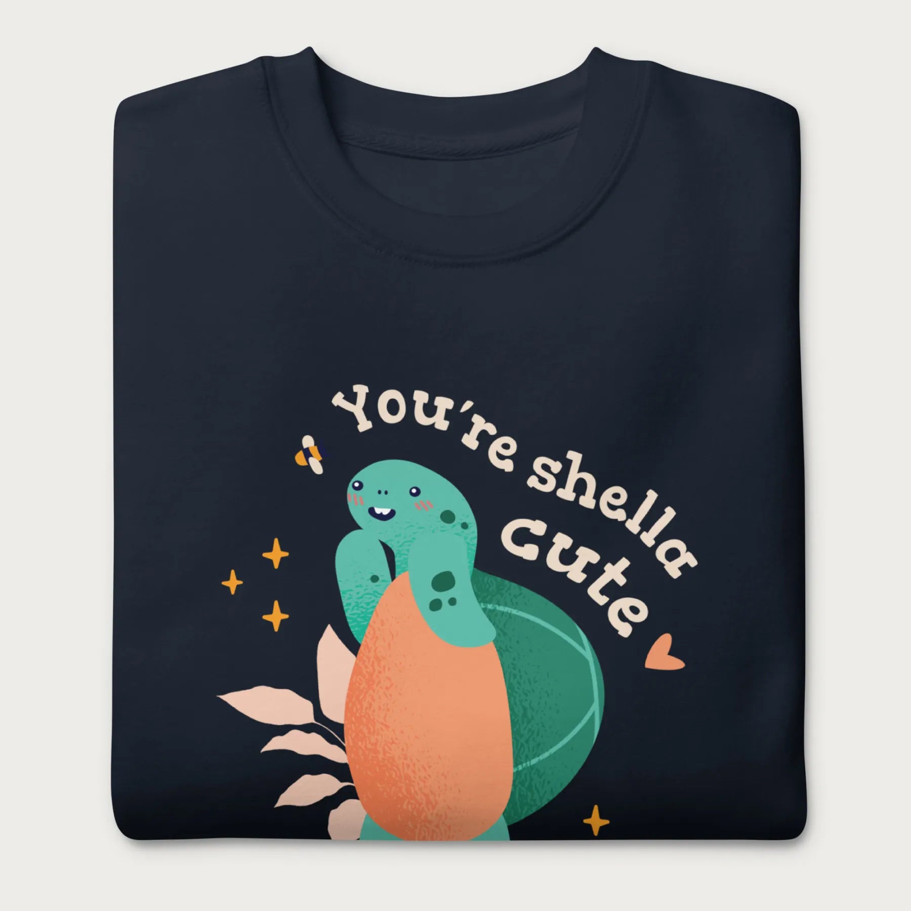 Folded navy blue sweatshirt with a cute graphic of a smiling turtle and bee with the phrase 'You're Shella Cute.'