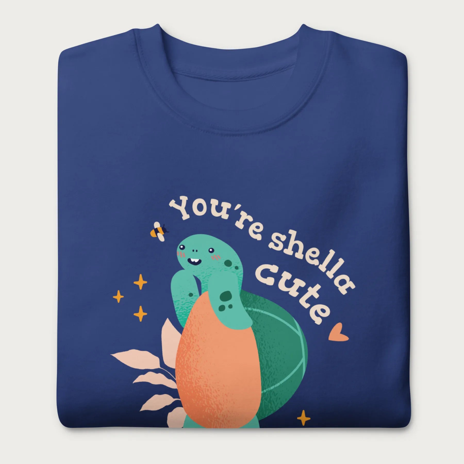 Folded royal blue sweatshirt with a cute graphic of a smiling turtle and bee with the phrase 'You're Shella Cute.'