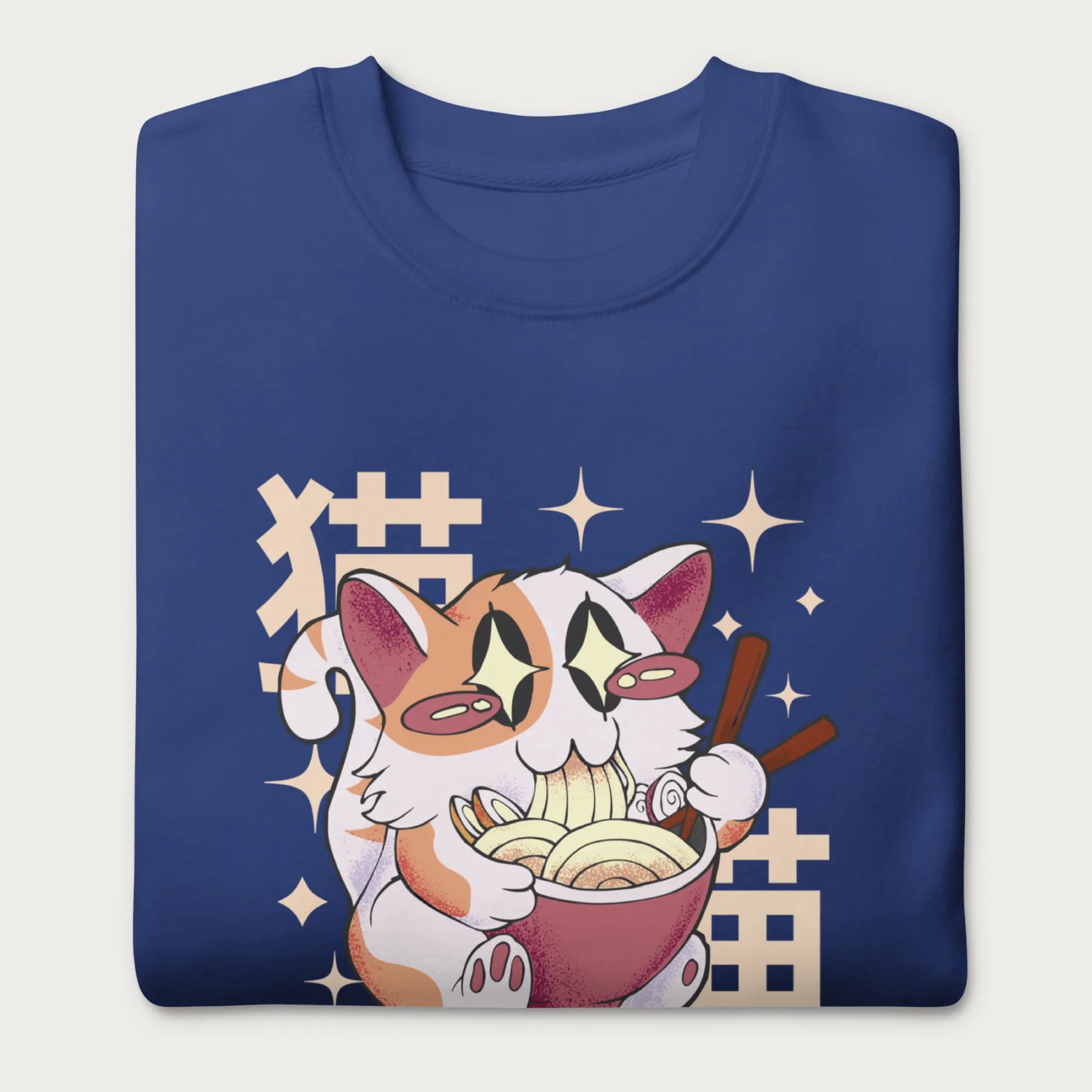 Folded royal blue sweatshirt with Japanese text and a graphic of a kawaii cat eating ramen.