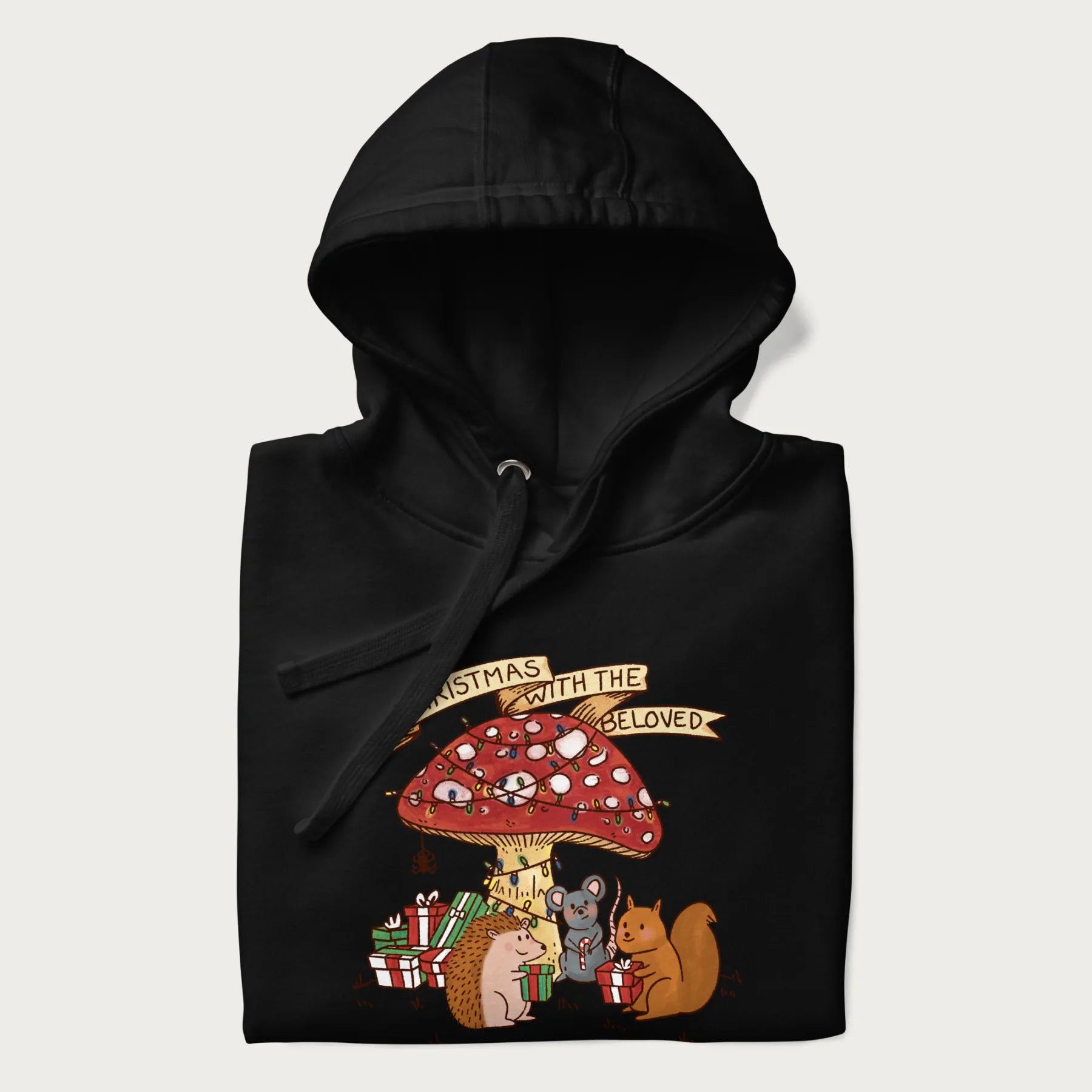 Folded black hoodie with animal around a festively decorated mushroom and the text 'Christmas with the Beloved' above.