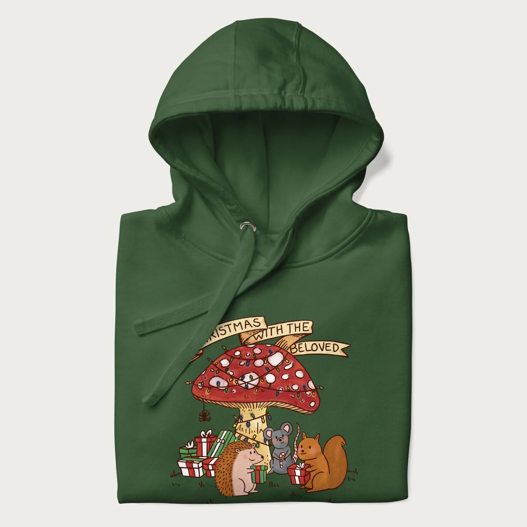 Folded forest green hoodie with animal around a festively decorated mushroom and the text 'Christmas with the Beloved' above.