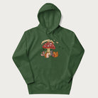 Folded forest green hoodie with animal around a festively decorated mushroom and the text 'Christmas with the Beloved' above.