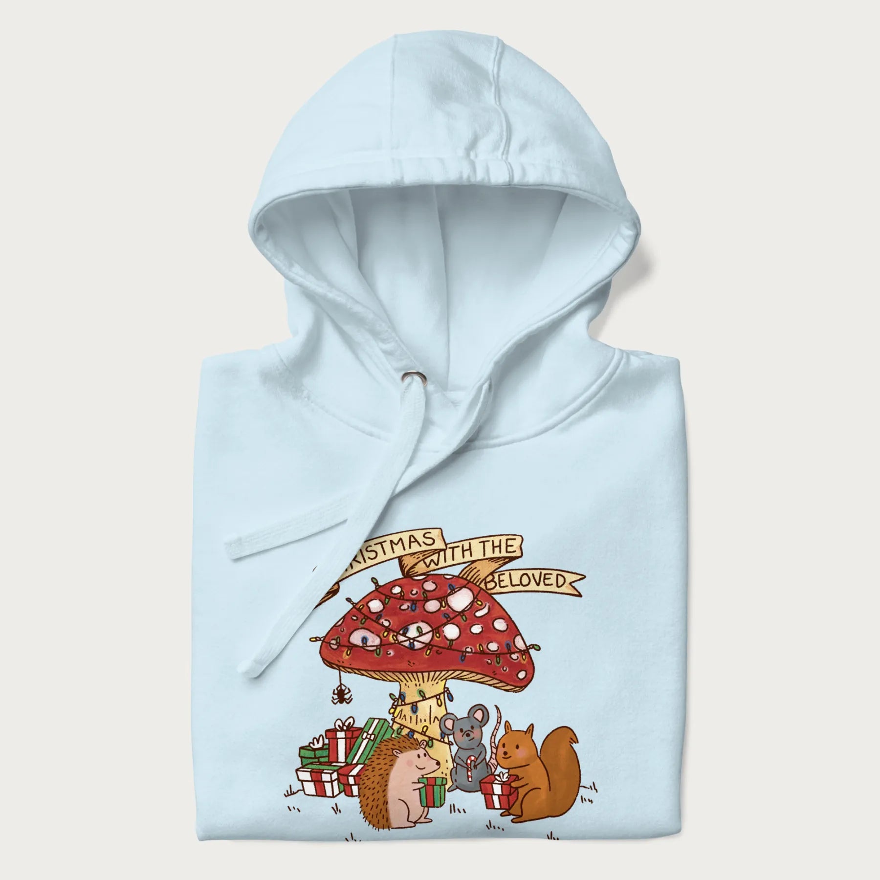 Folded light blue hoodie with animal around a festively decorated mushroom and the text 'Christmas with the Beloved' above.