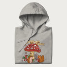 Folded light grey hoodie with animal around a festively decorated mushroom and the text 'Christmas with the Beloved' above.