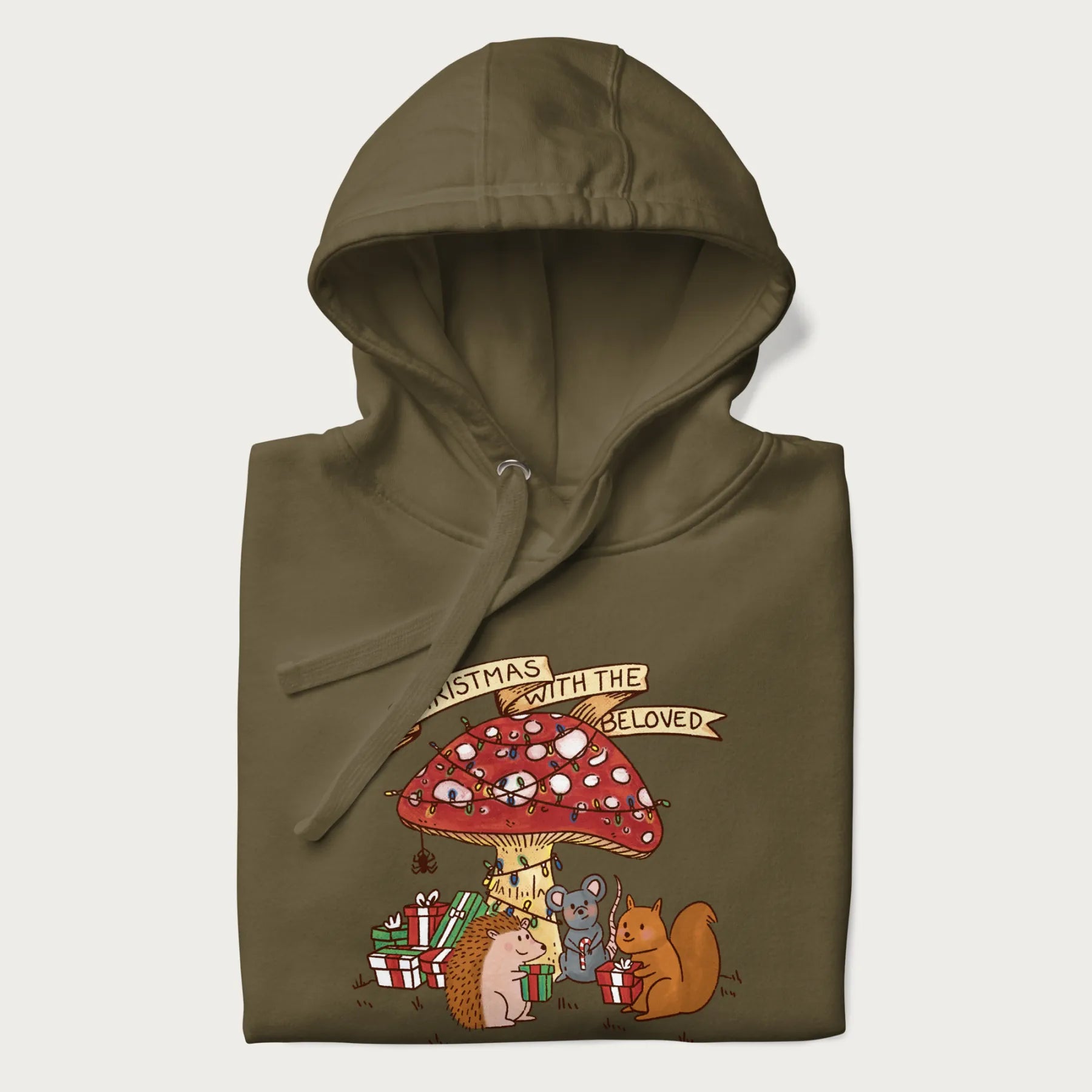 Folded military green hoodie with animal around a festively decorated mushroom and the text 'Christmas with the Beloved' above.