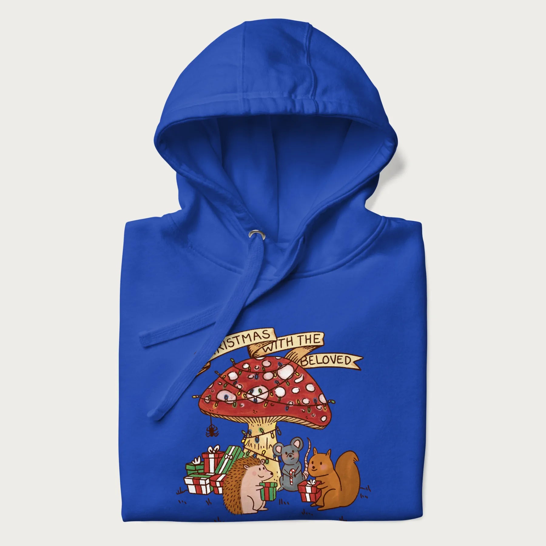 Folded royal blue hoodie with animal around a festively decorated mushroom and the text 'Christmas with the Beloved' above.