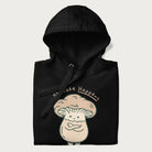Folded black hoodie with a graphic of an adorable mushroom character and the text 'Shiitake Happens'.