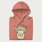 Folded light pink hoodie with a graphic of an adorable mushroom character and the text 'Shiitake Happens'.