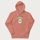 Light pink hoodie with a graphic of an adorable mushroom character and the text 'Shiitake Happens'.