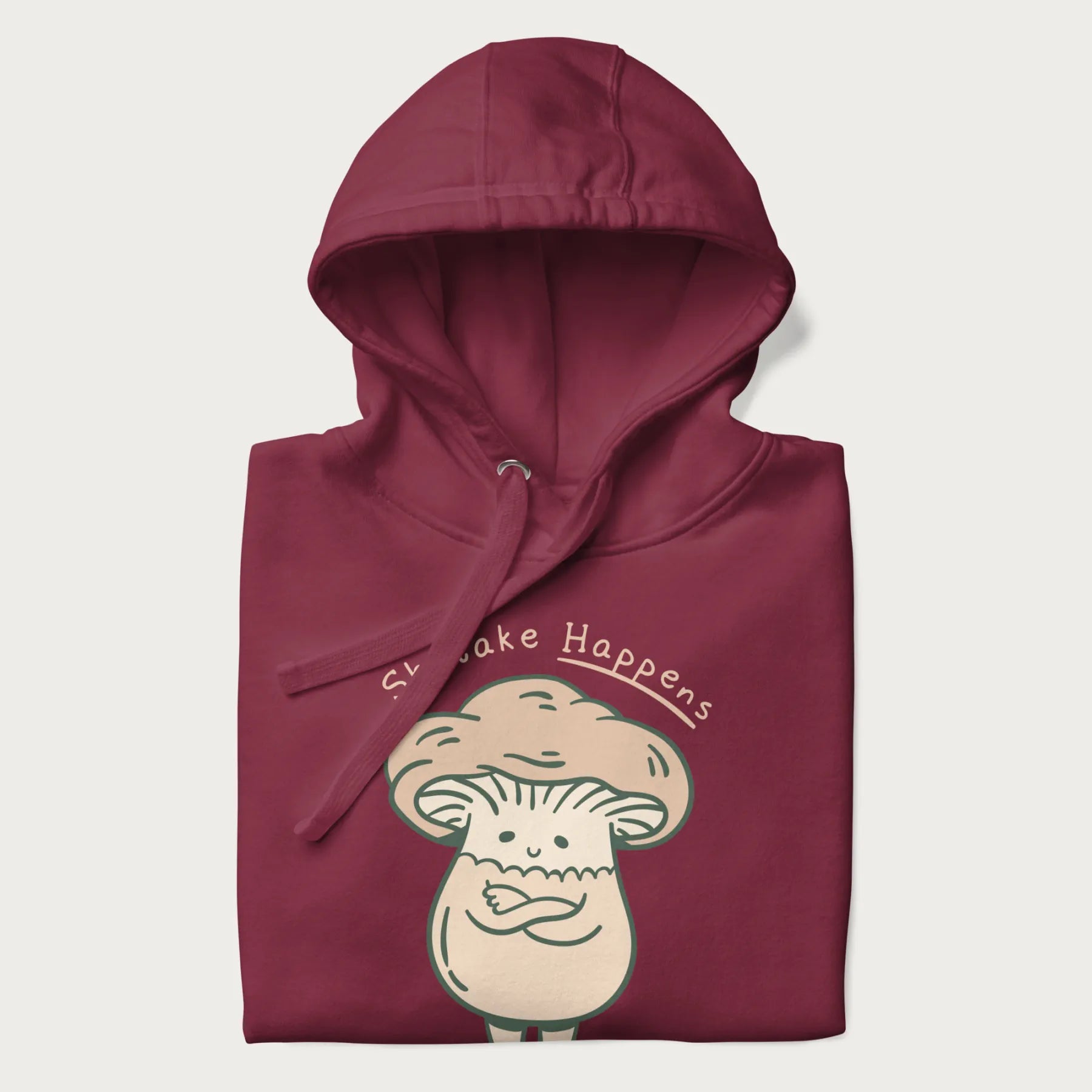 Folded maroon hoodie with a graphic of an adorable mushroom character and the text 'Shiitake Happens'.