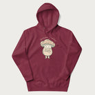 Maroon hoodie with a graphic of an adorable mushroom character and the text 'Shiitake Happens'.